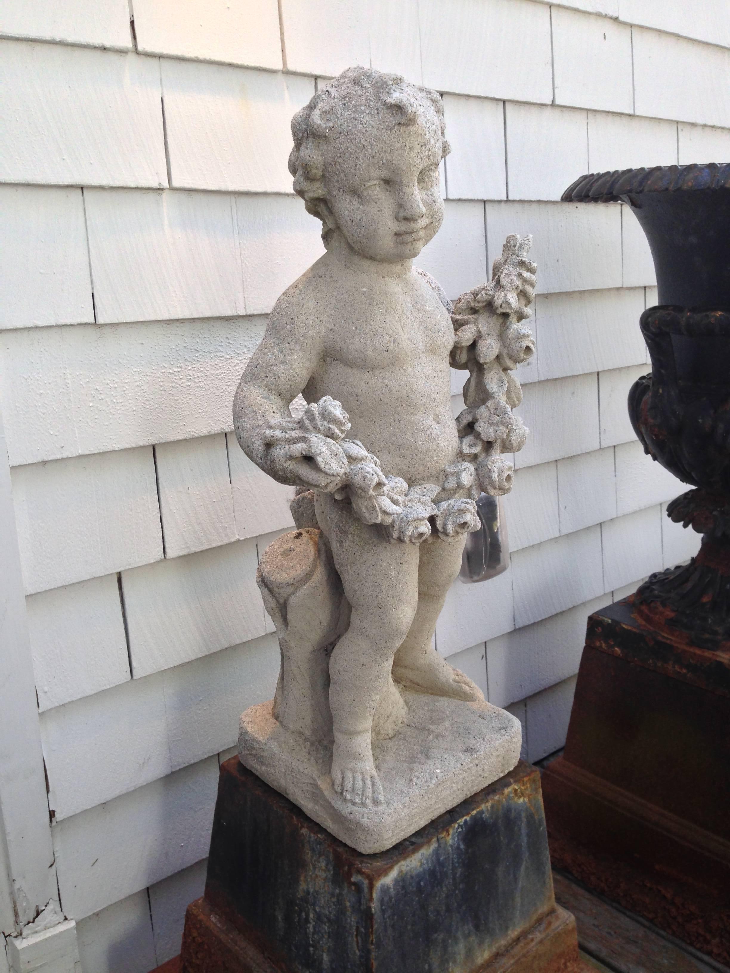 An early 20th century cast stone statue of a putto holding a delicate floral garland.
