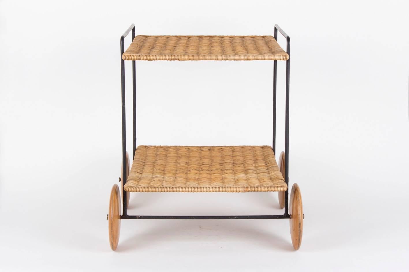 A marvelously preserved serving trolley designed by Carl Auböck in his famous workshop in Vienna.

The shelf’s made of handwoven wicker, the frame produced in painted metal, wheels made of beechwood with the typical brass knobs.

Illustrated