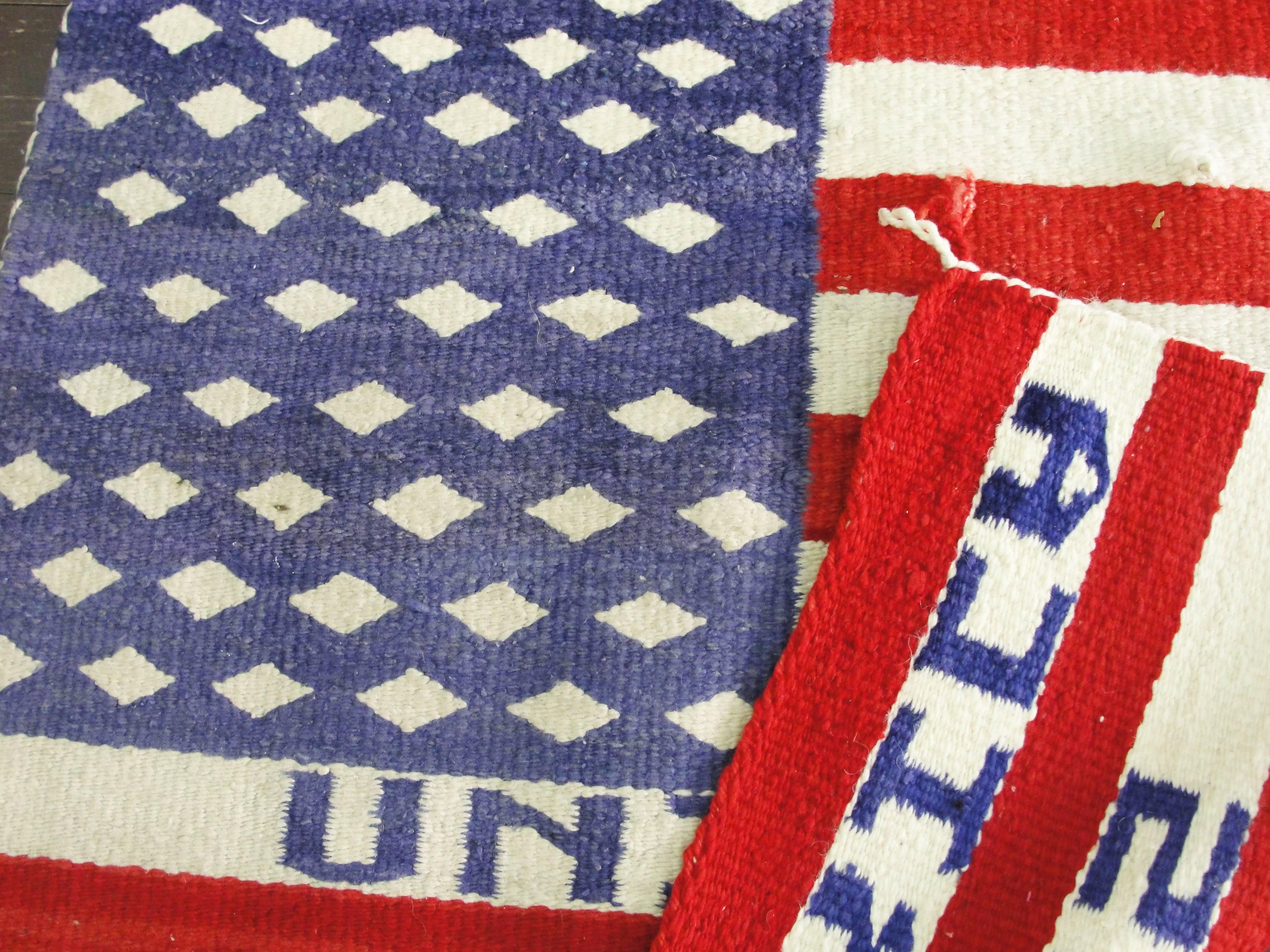 Pictorial Navajo rug depicting U.S. flag with 50 white diamonds representing the stars on a bluish/purple field with red and white stripes. United States of America woven into the red and white strips.
