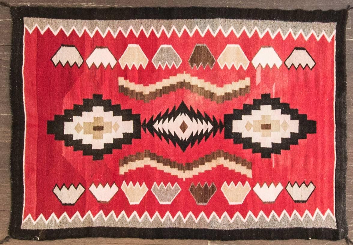 This early 20th century Navajo rug features the Red Mesa motif, bordered with jagged zigzag patterns. Red Mesa was a trading post in Arizona, and the rugs from this outfit were known for their precision and intricacy. This is a 'pound' rug, dating
