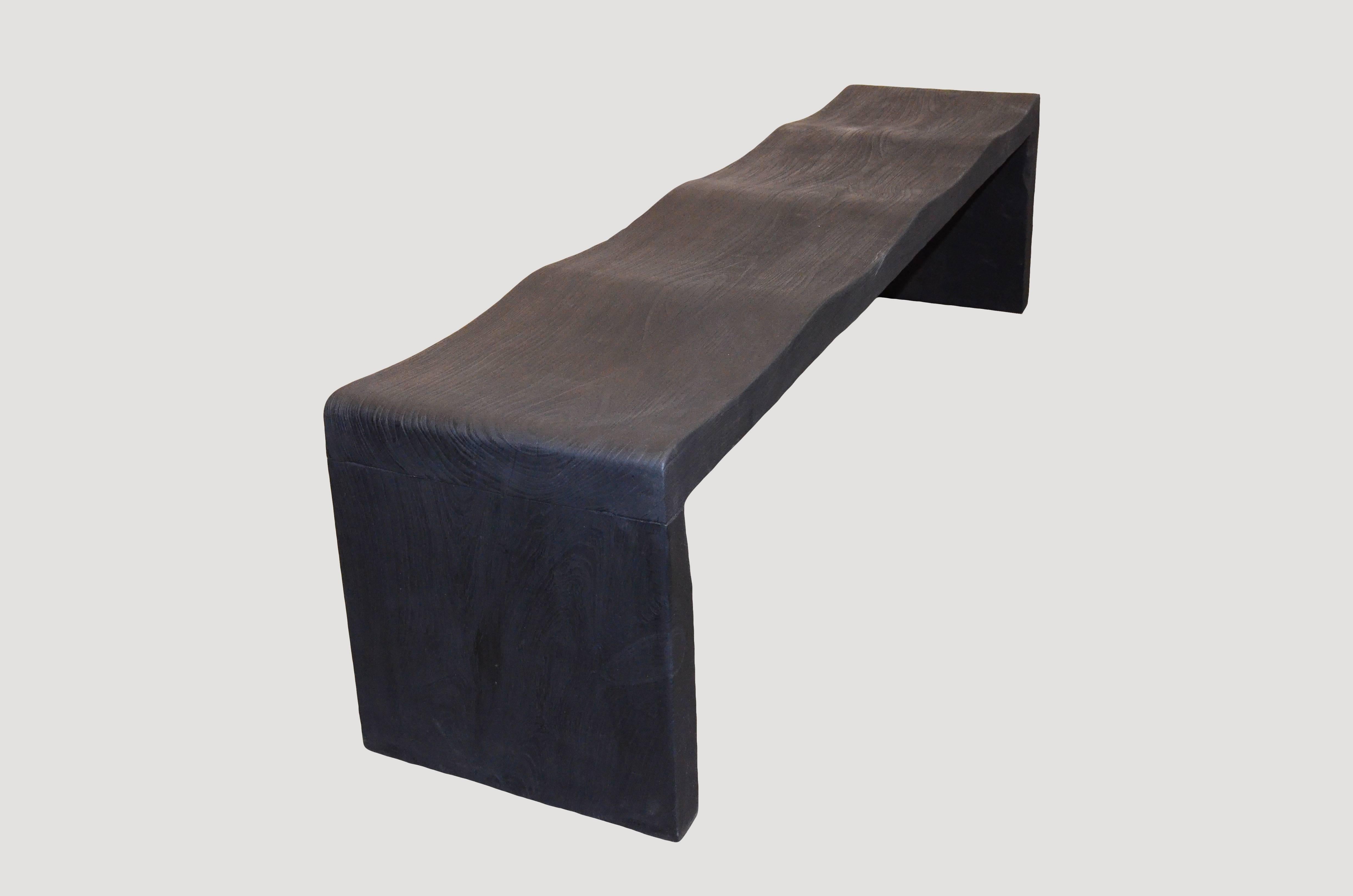 The teak wave bench represents a sleek, modern aesthetic, designed to provide comfort and durability. Solid reclaimed teak wood is hand carved into a wave design. Burnt, sanded and sealed with a smooth finish. Available in matte and gloss finishes.