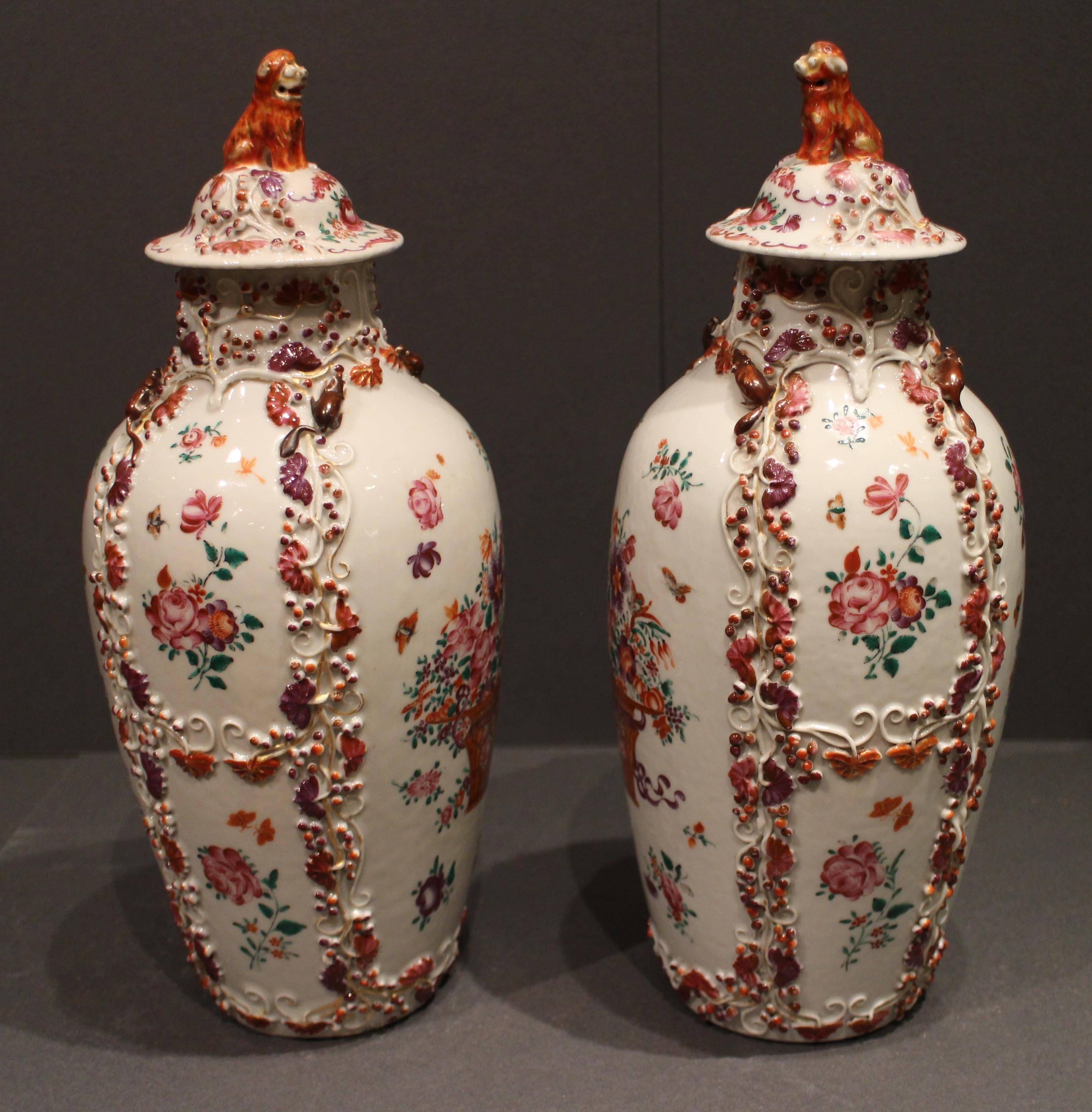 A pair of antique Chinese famille rose vases, decorated with floral displays in pinks, purples and oranges and applied three-dimensional flowers and squirrels, the lids topped with orange foo dogs.