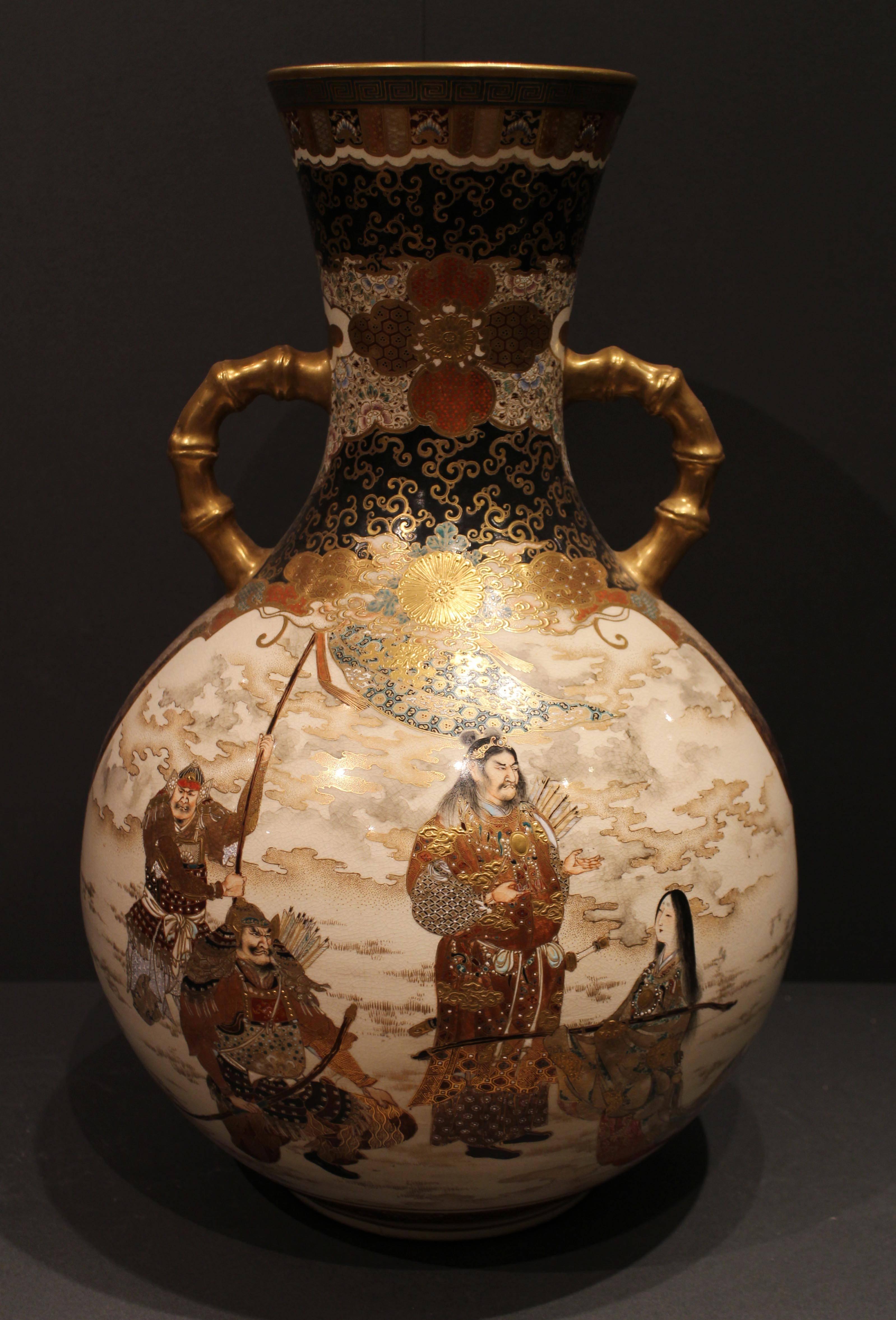 A large round antique Japanese Satsuma pottery vase, decorated in a cream, gold and orange panels of samurai warriors and bijin, on a dark blue and gold ground, the neck decorated with complex patterns, the handles of the vase are in the form of