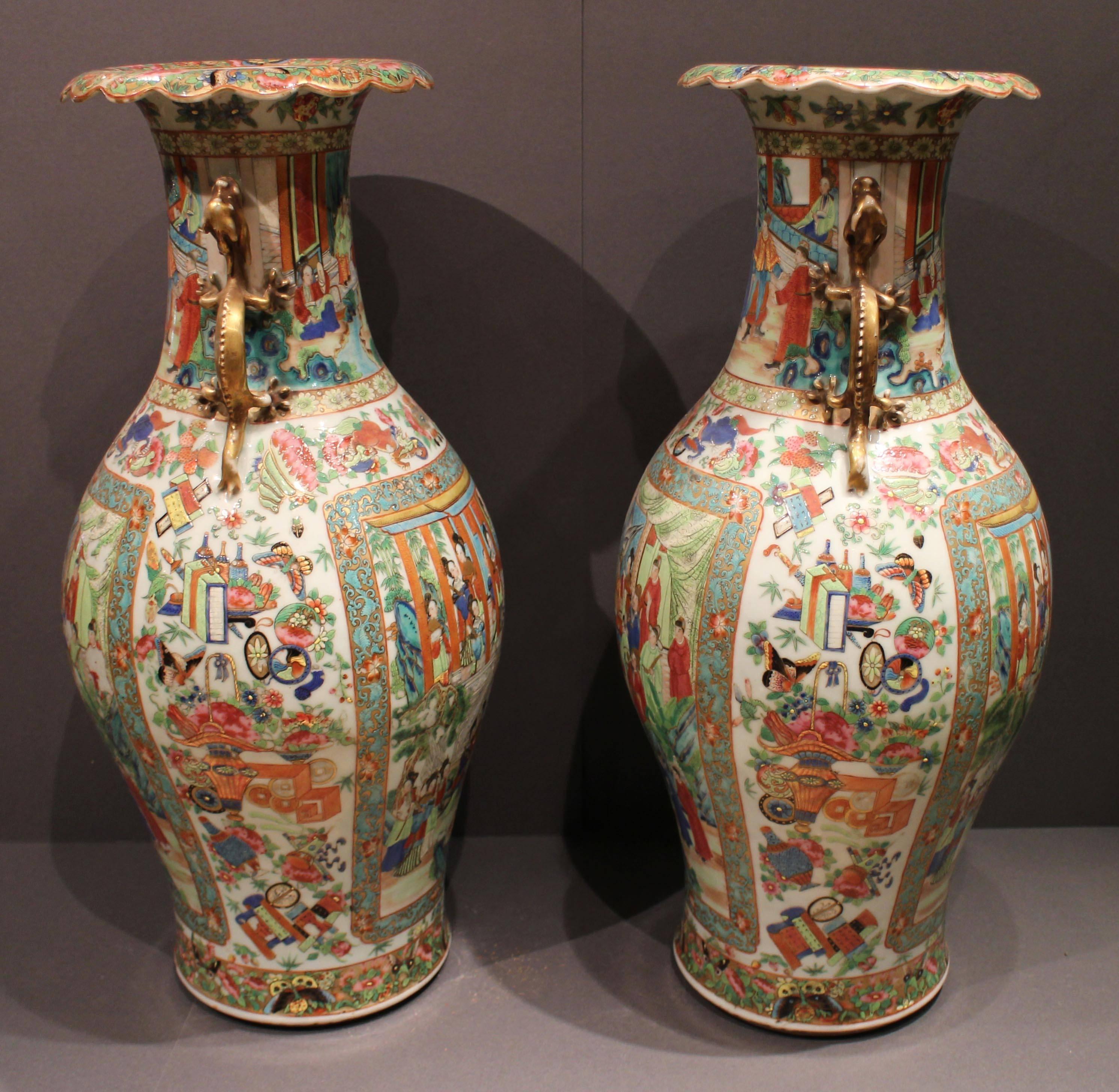A pair of large antique Chinese Cantonese vases with golden dragon ears, the vases are decorated with a bold and colorful design of precious objects on a cream background, and large panels in the traditional Canton color pallet, depicting meetings