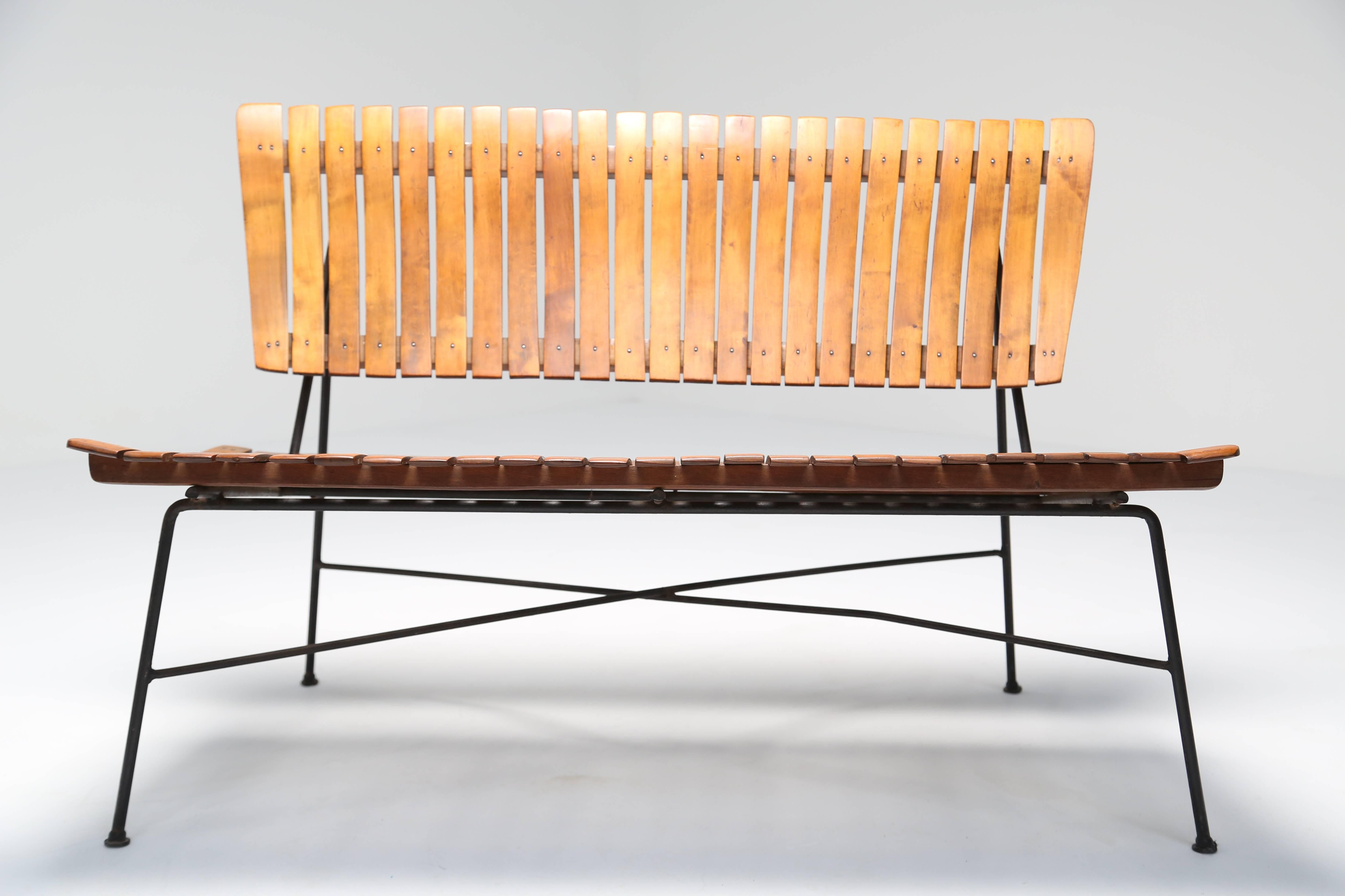 Arthur Umanoff slatted wooden bench with black wrought iron frame, circa 1955. Wood slats are possibly Birch and have a beautiful honey color. Its a stunning piece in person and given the right location it could be the centrepiece of that space.