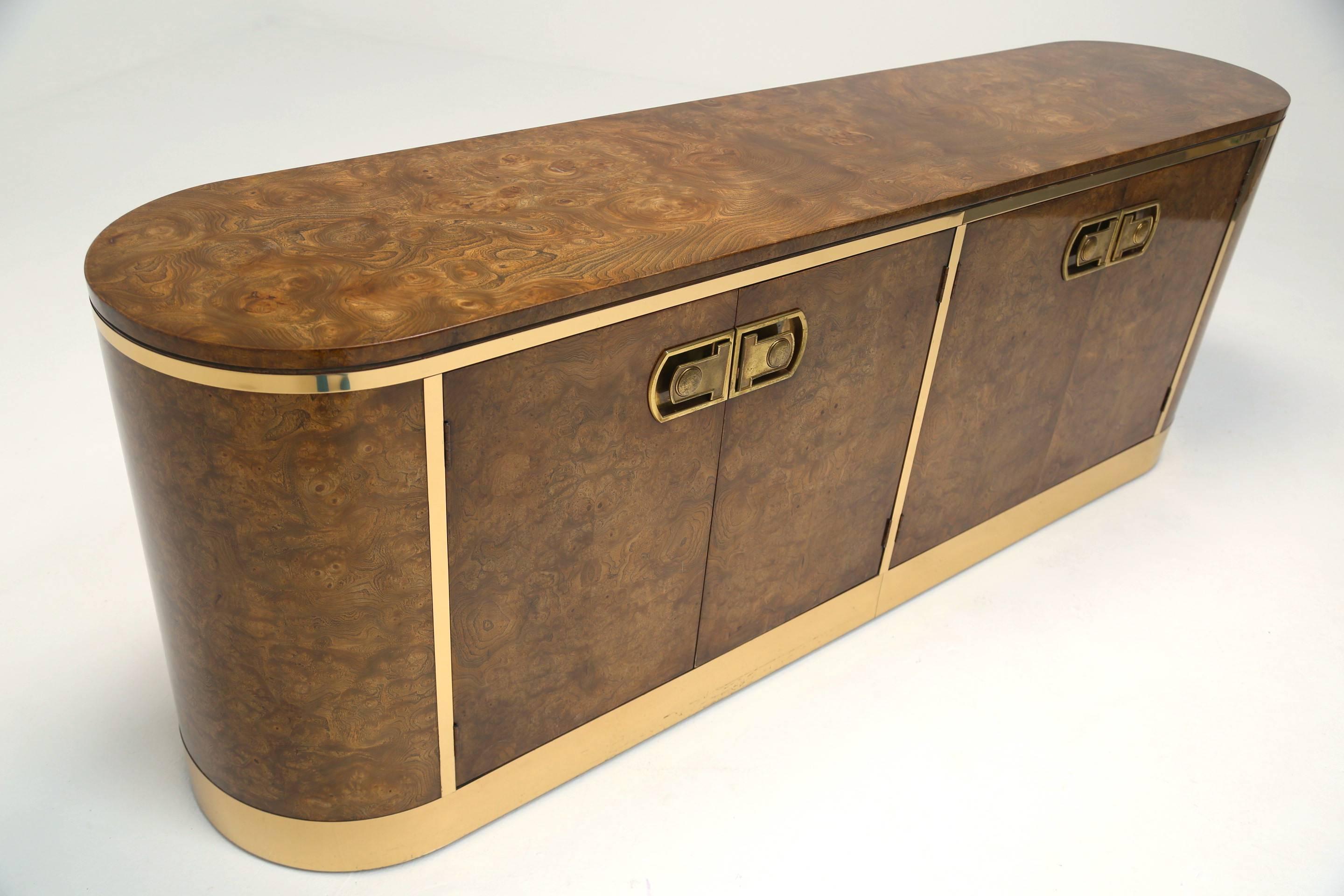 This stately and handsome sideboard by Mastercraft uses a warm walnut burl, brass appointments and polished brass edging to finish this piece. It has three beautifully crafted concealed drawers to the left and two deep shelves behind the right hand