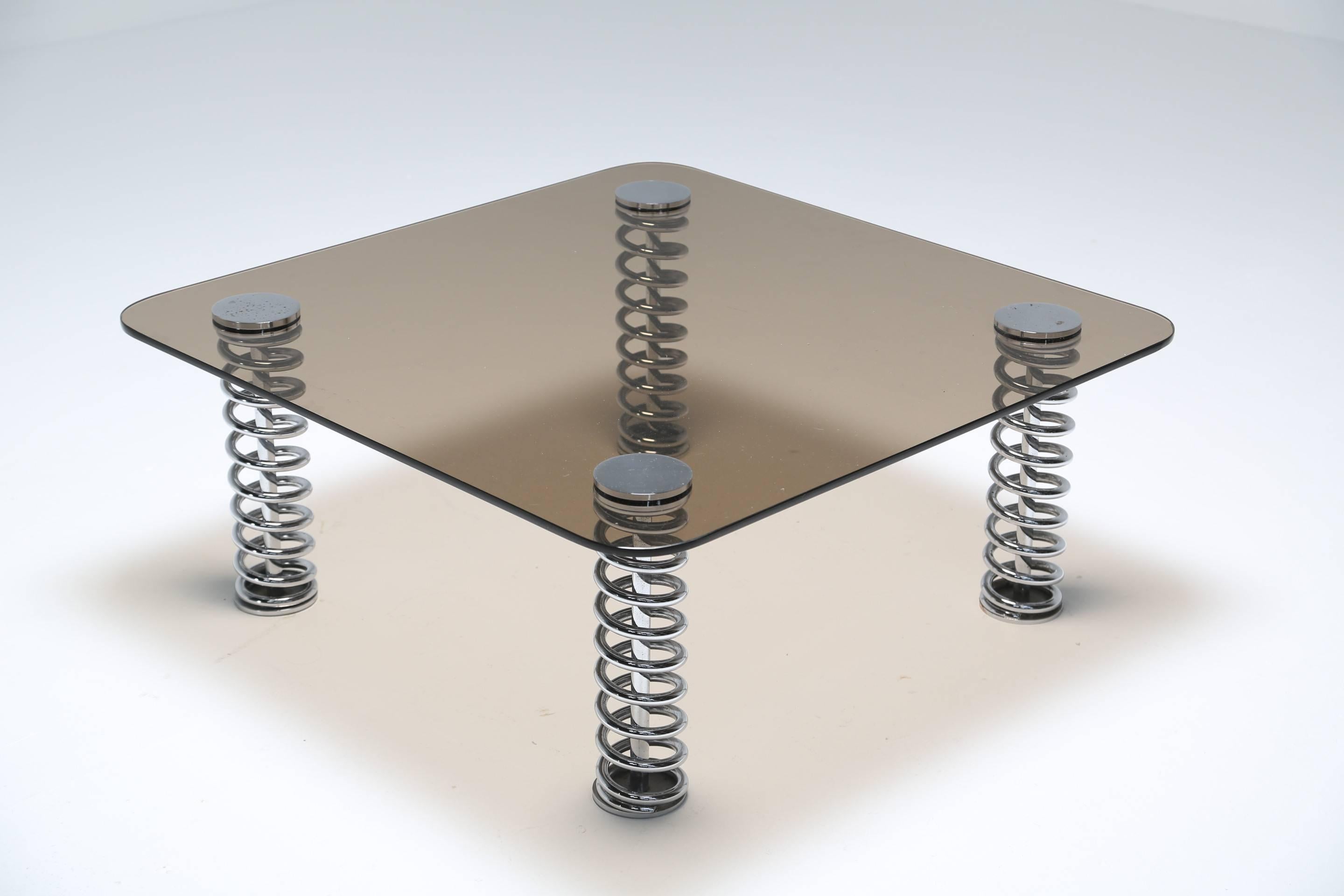 A smoked glass tabletop mounted on four rigid chrome springs. The table is very solid and does not move on the springs. This might make a good piece for a car enthusiast or in a man cave. Unknown maker but possibly British.