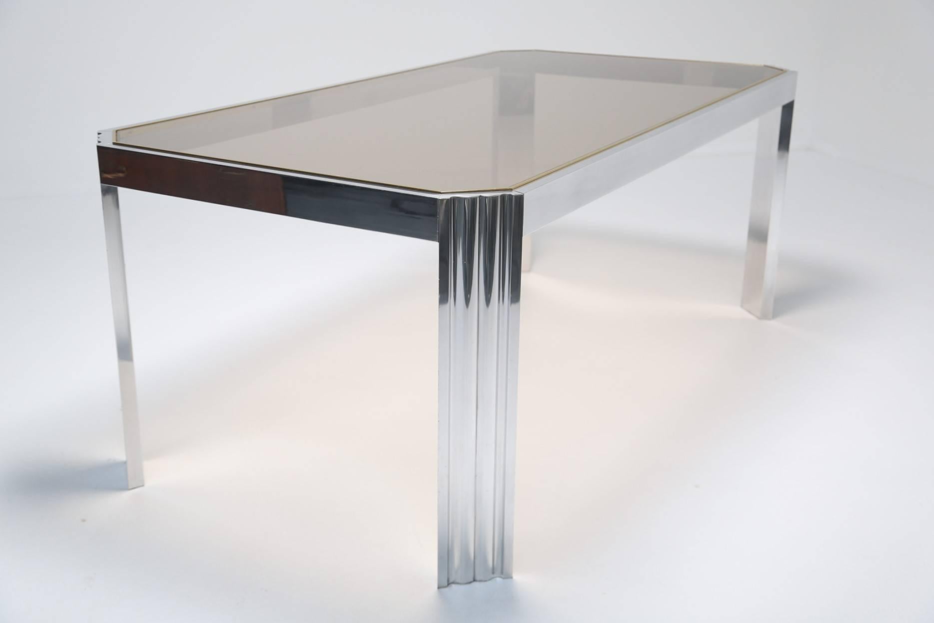 A very elegant and simple aluminum dining table with glass top and a delicate brass trim which frames the glass top beautifully. The table looks chrome but is in fact polished aluminum which means it  is easy to keep shiny and clean. The table has