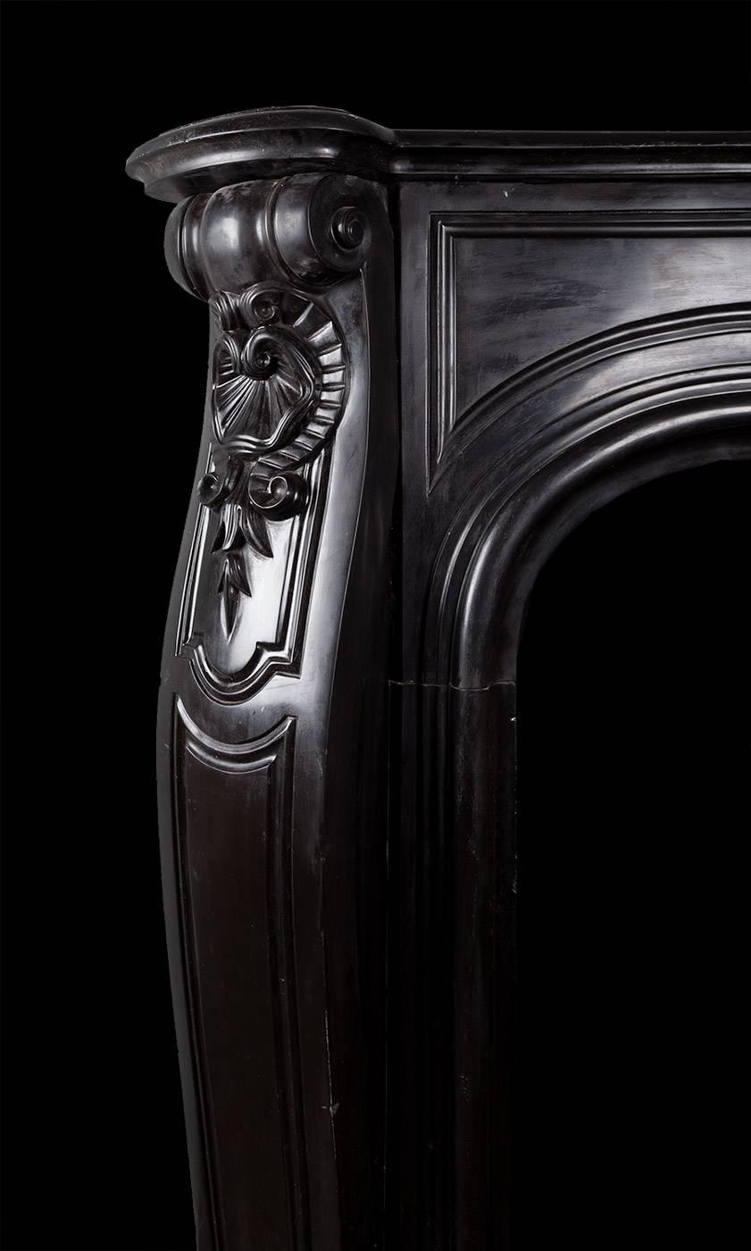 Antique Louis XV style fireplace in Belgian black marble

The deep moulded mantelpiece rests above a panelled serpentine frieze, which is centred by a carved Rococo style clam shell cartouche. The panelled consoles are canted and carved with