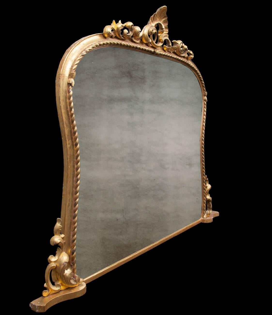 Large antique Irish carved giltwood overmantel mirror. The rope twist decorated shaped frame, surmounted by an ornate foliate pediment with flanking carvings to the base. The original gilding is a great color and the overall condition of the mirror