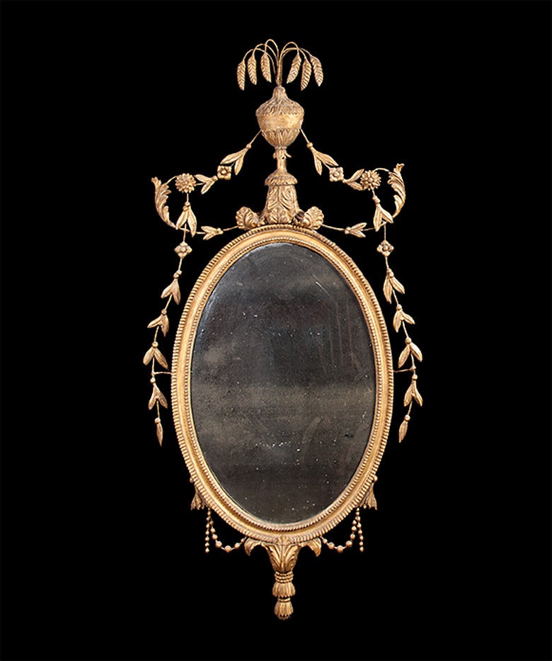 A very fine pair of late 18th century neoclassical, carved and giltwood oval mirrors with original plates. The beaded oval frames have tall classical urns capped with ears of wheat, whilst laurel leaves and berries descend down each side.