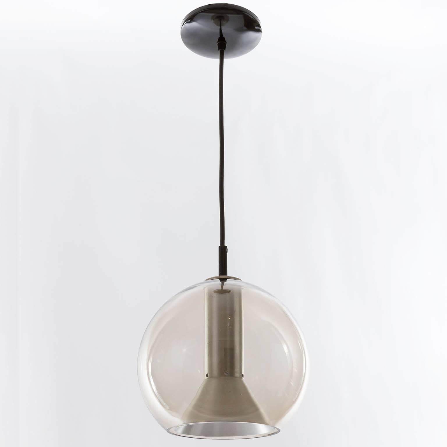 A set of three pendant lights / hanging lamps by Frank Ligtelijn for RAAK Amsterdam, Netherlands, manufactured in the 1960s. They are made of smoked glass globes with aluminum shades. One medium Edison base bulb E26 / E27 per light. A cord in any