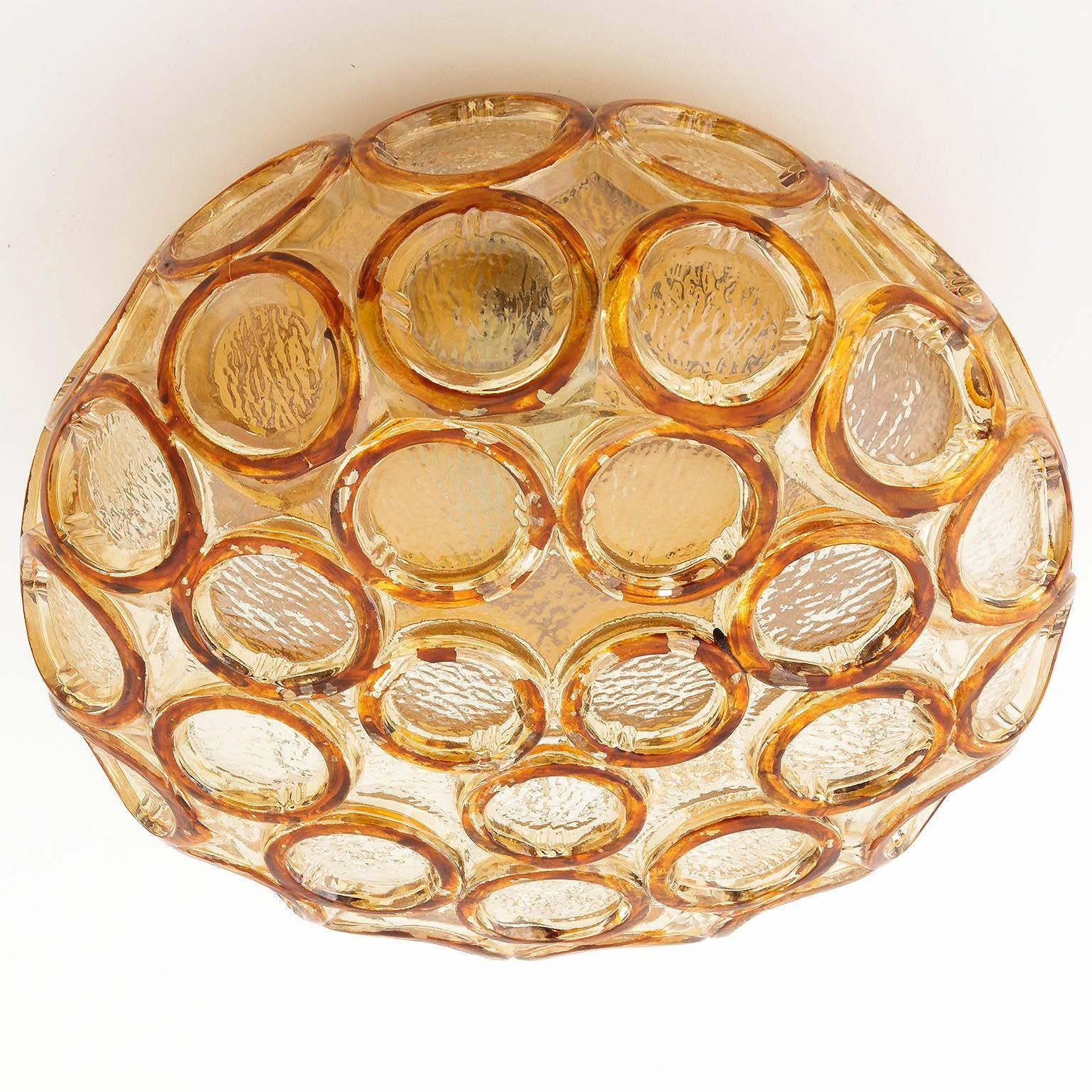 A set of three amber tone glass light fixtures in the style of Limburg, manufactured in Mid-Century (1960s-1970s). They can be used as wall or ceiling lamps. Each lamp is an original vintage piece with some flaking to the colored rings and a gold