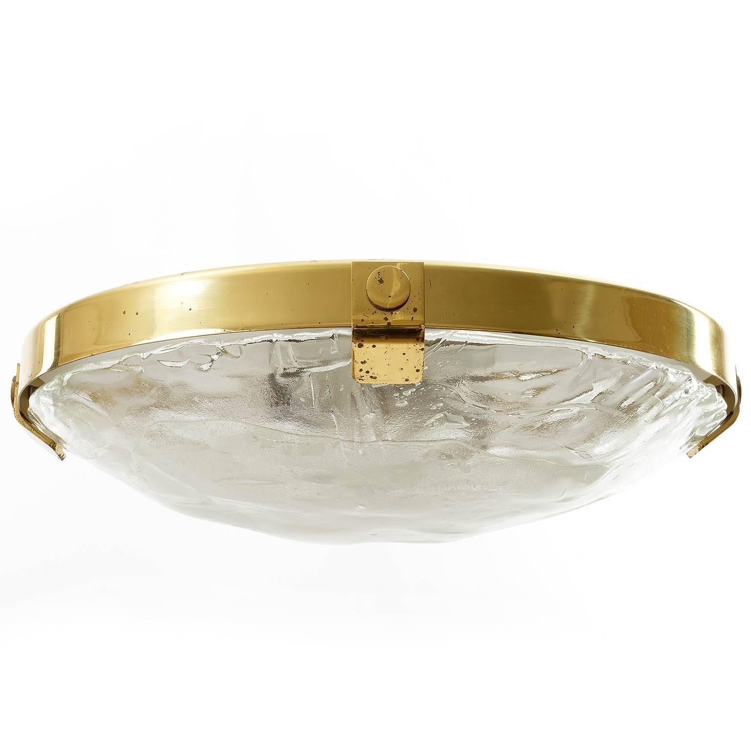 One of three brass and Murano glass flush mount light fixtures by Kalmar, manufactured in Mid-Century, circa 1970 (late 1960s or early 1970s).
It is made of a brass ring which holds a large hand blown glass with four brass brackets. The glass has a