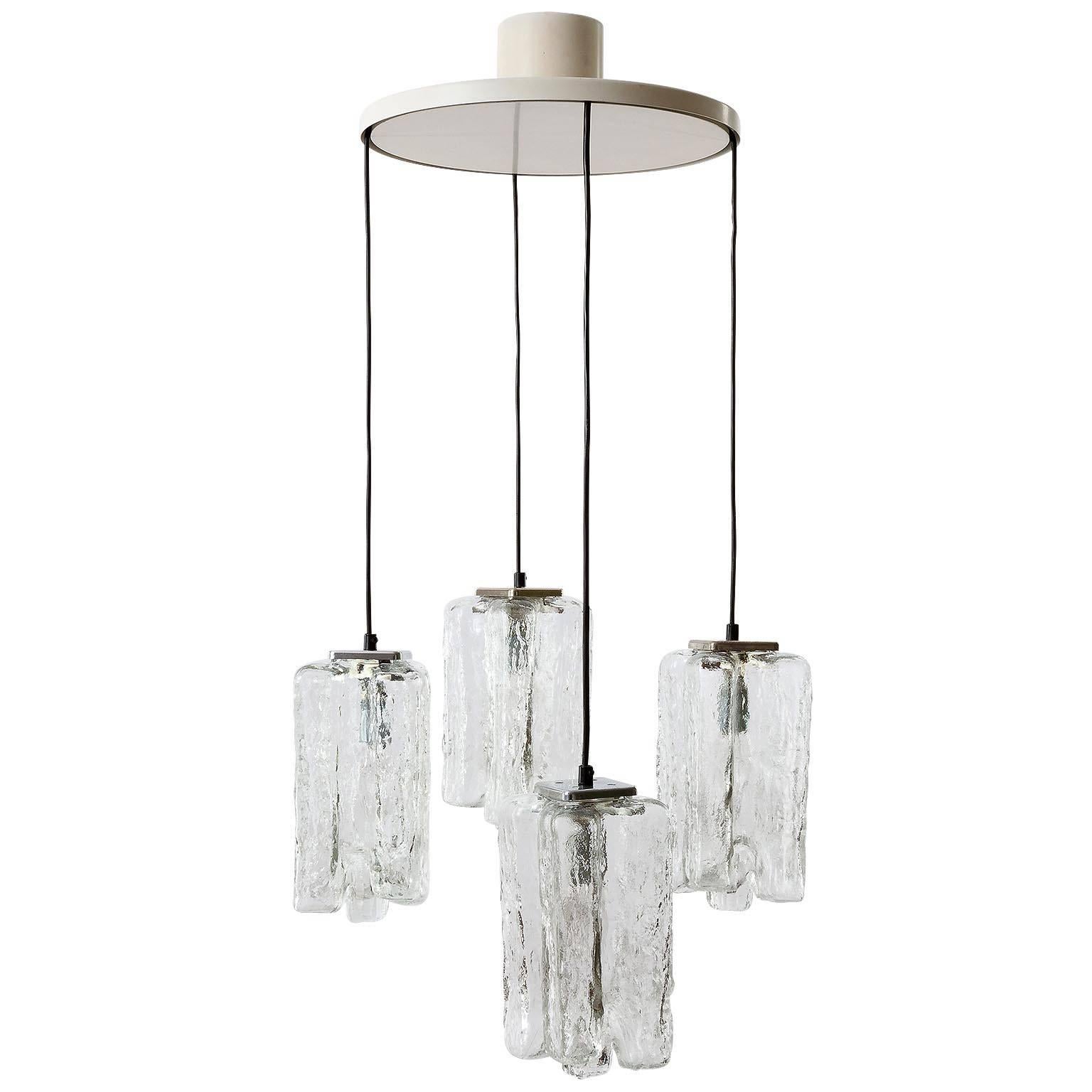 A hanging lamp by Kalmar, Austria, manufactured in Mid-Century, circa 1970 (late 1960s or early 1970s). It is made of four frosted ice glass lamp shades which are hanging on a white painted ceiling plate. The cords are adjustable in height.
Each