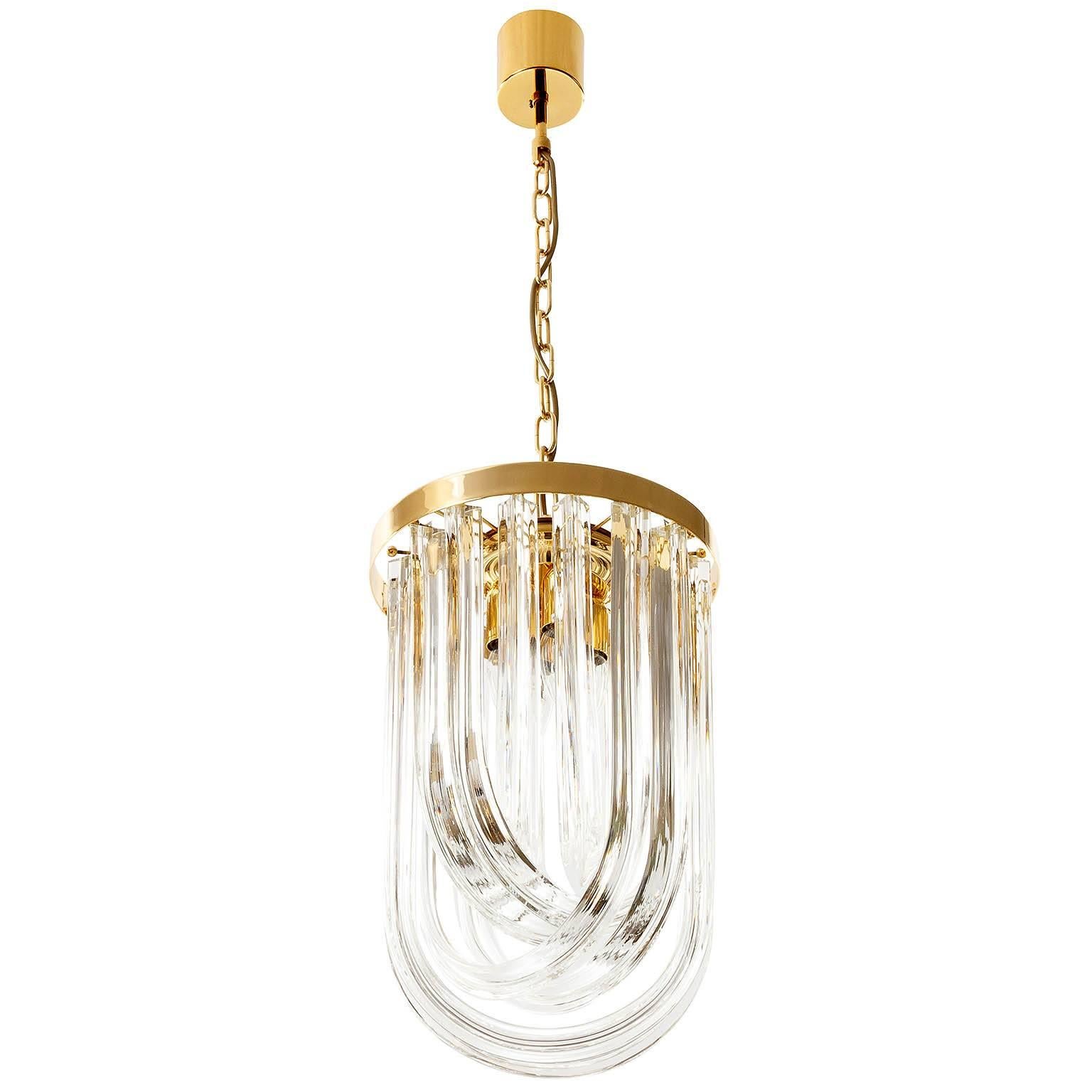 A wonderful Italian hollywood regency pendant light by Venini manufactured in Mid-Century in the 1960s. It is made of pairwise curved crystal Murano glasses in different lengths and a gold-plated brass frame. Excellent condition.
The height of the