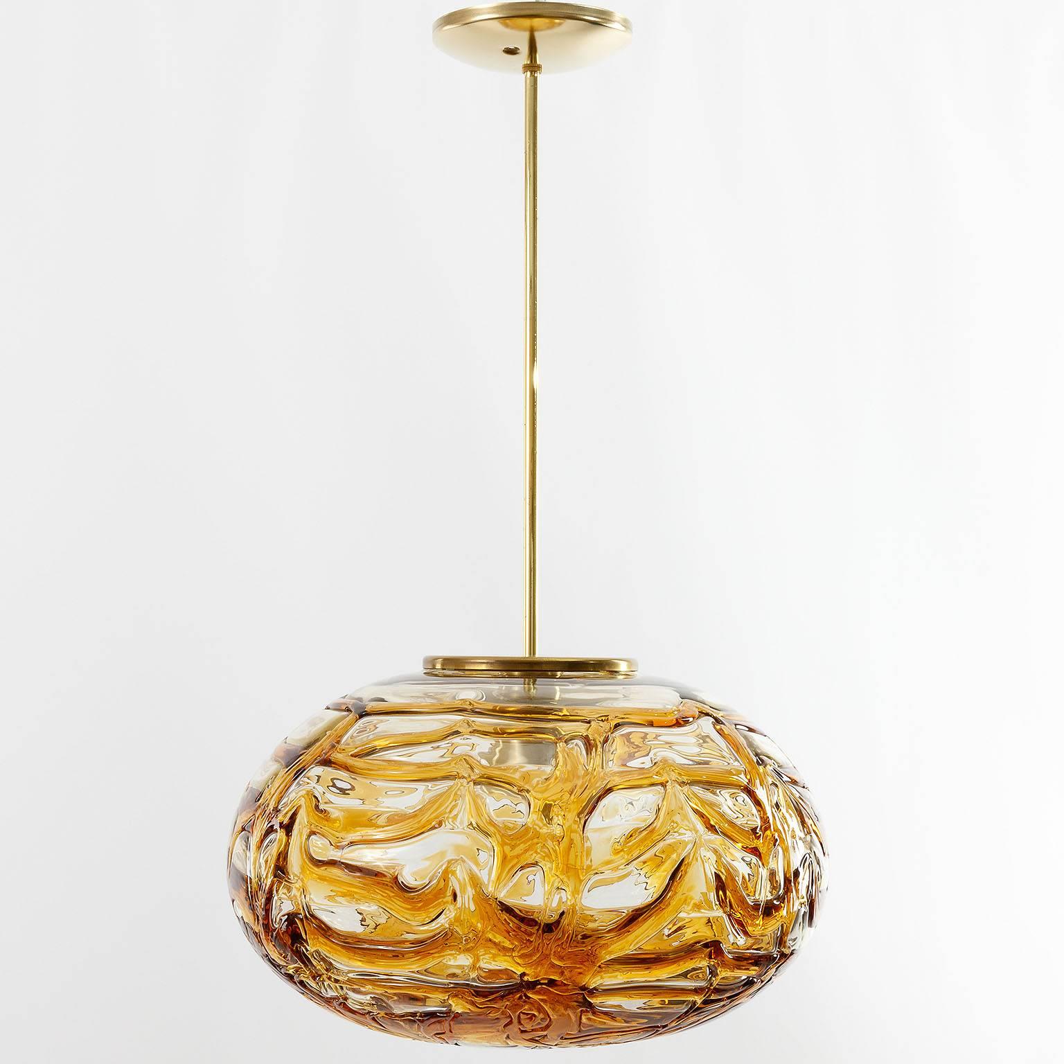 A fantastic textured glass pendant light by Doria Leuchten Germany manufactured in Mid-Century, ca. 1970 (end of 1960s and beginning of 1970s). A large and thick oval glass globe with a texture made of melted orange / amber tone glass.
The stem and