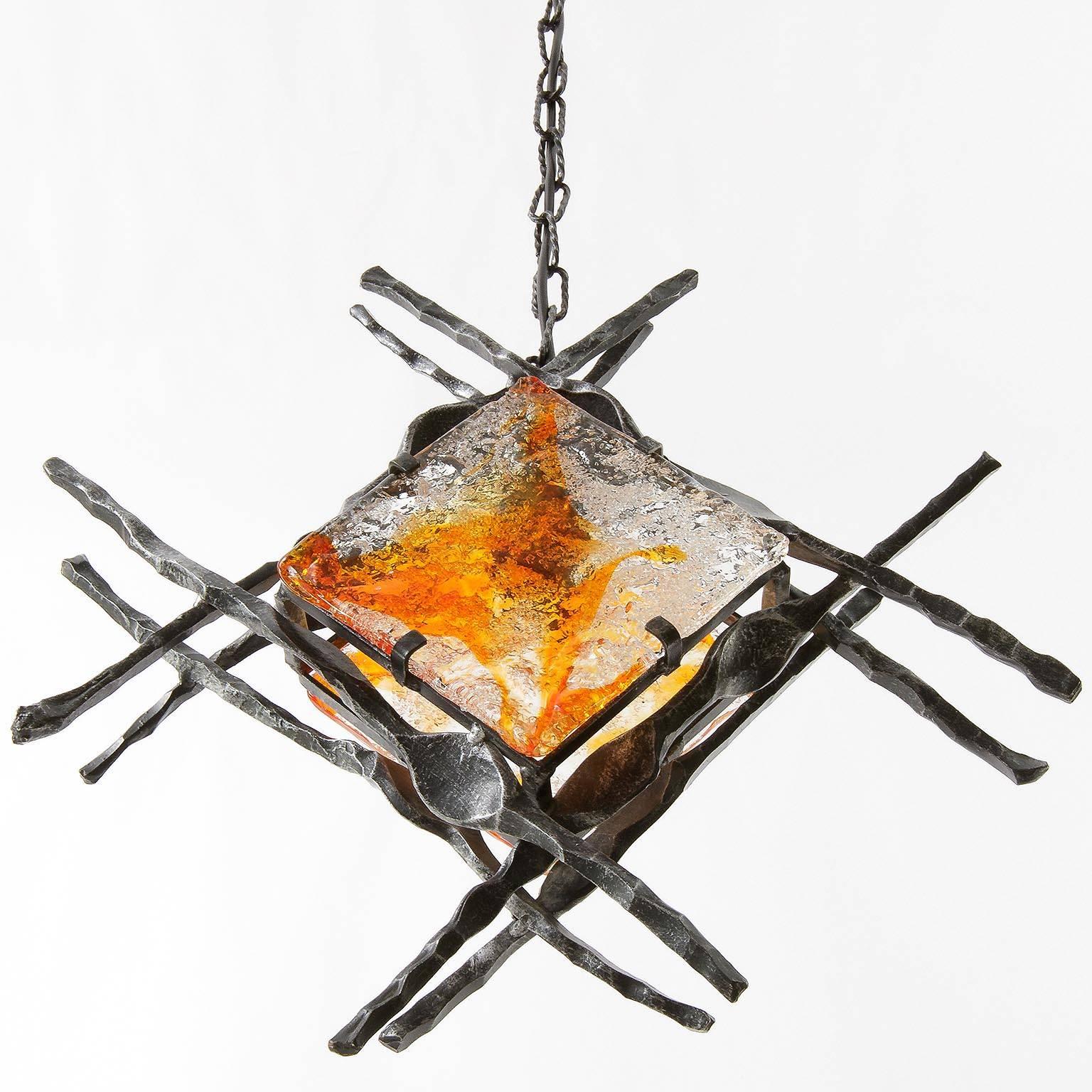 A Brutalist style handmade iron and glass light fixture, manufactured in Mid-Century, circa 1970. 
This modernist lamp is made of wrought iron and two handblown orange / amber tone glasses.
It can be used as pendant or wall light. The light has one