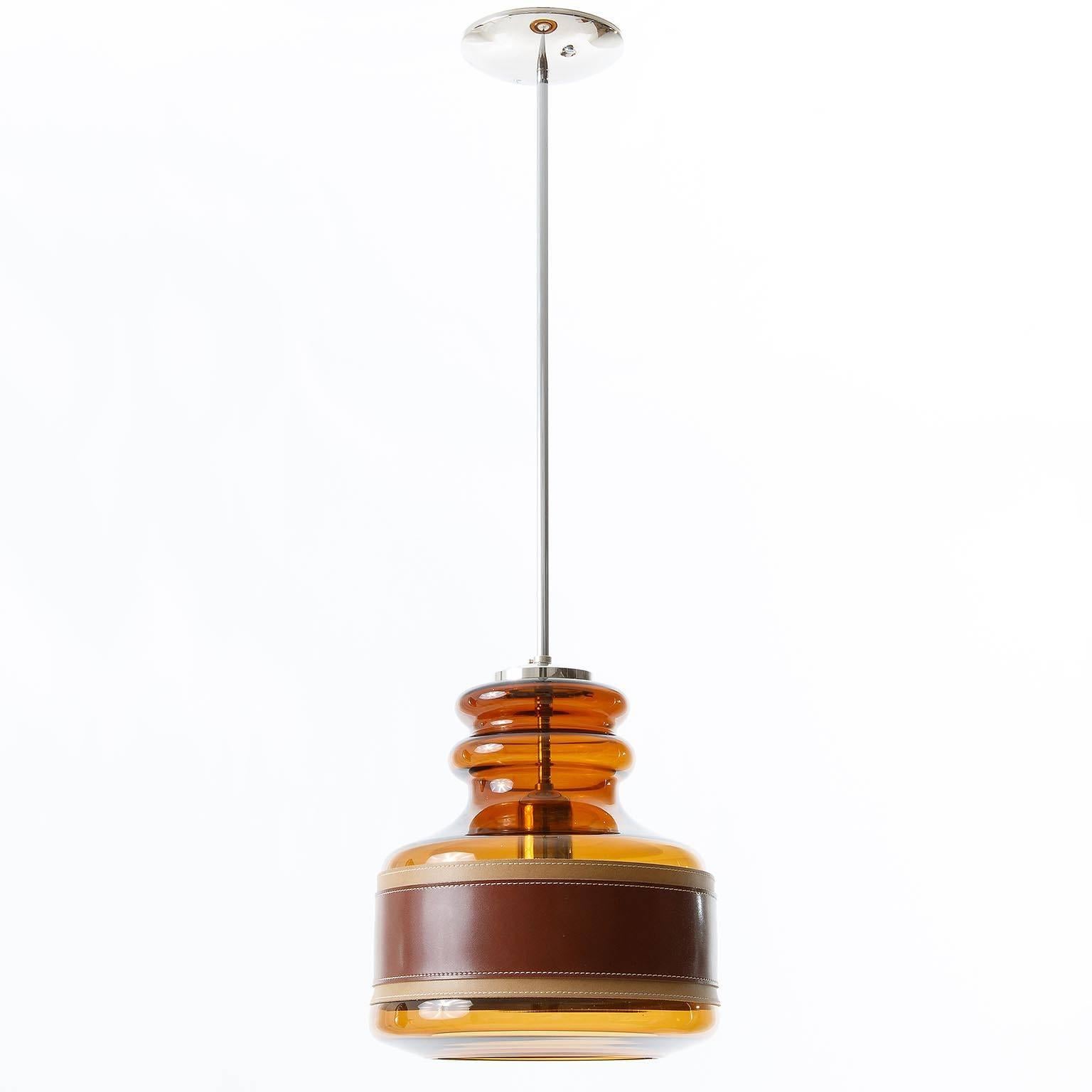 A beautiful and very rare glass pendant light or chandelier by Kalmar, manufactured in Mid-Century, circa 1970 (late 1960s or early 1970s). It is made of a chromed hardware and an amber toned glass body with a belt made of two layers of brown