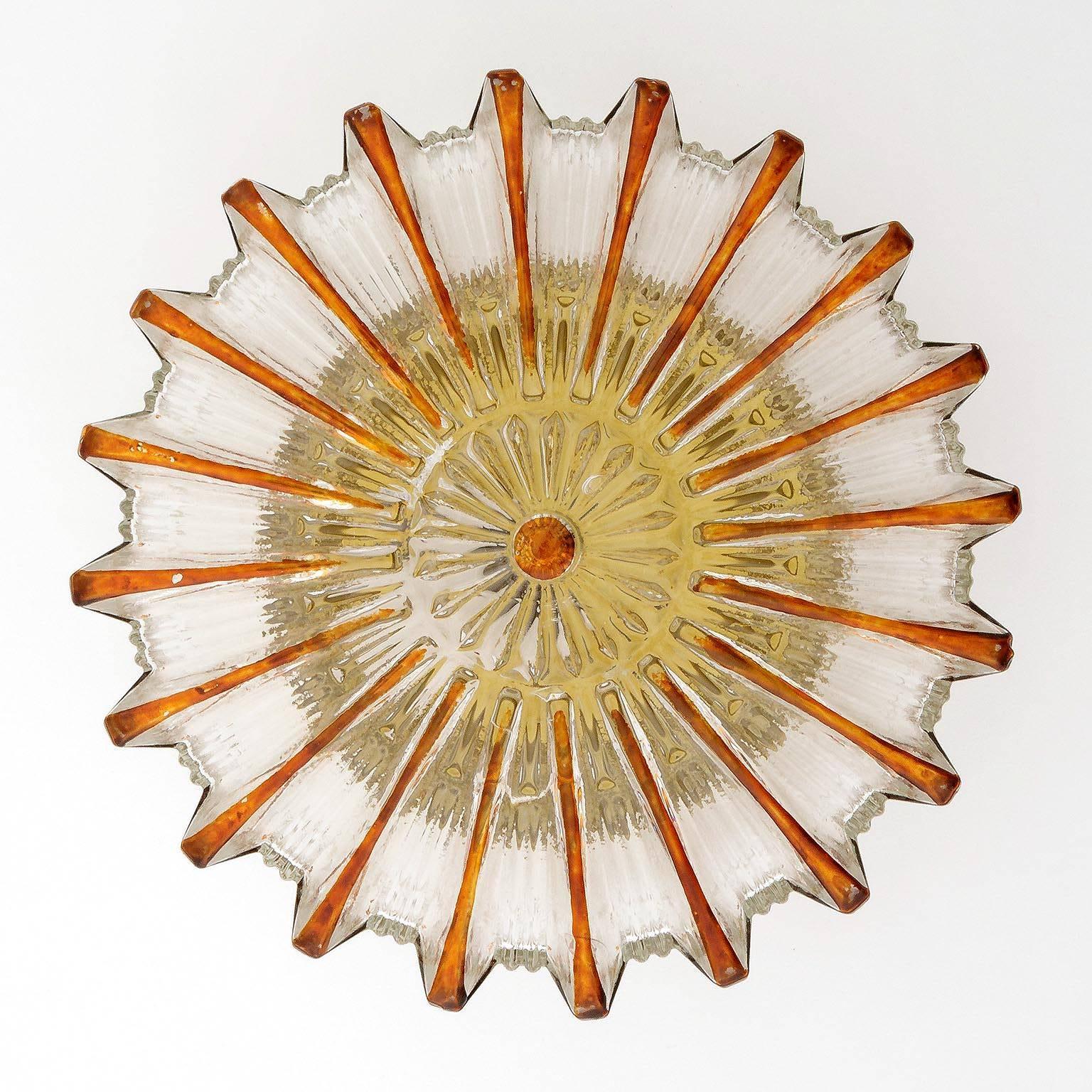 A vintage pair of glass flush mount sunburst sconces, manufactured in Midcentury, circa 1970 (end of 1960s and beginning of 1970s). Glass shades with amber tone rays and gold toned circular back plate. Some flaking to the colored rays.