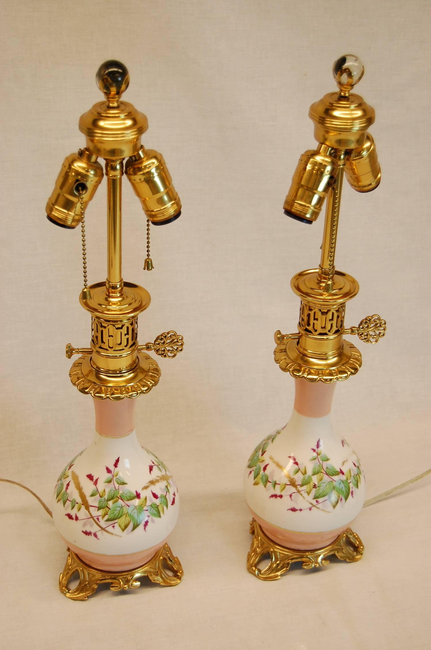 Pair of beautiful oil lamps wired on original gilt finished bases and caps. Pink bands and vines of leaves and burgundy flowers encircle the vase. Excellent condition.