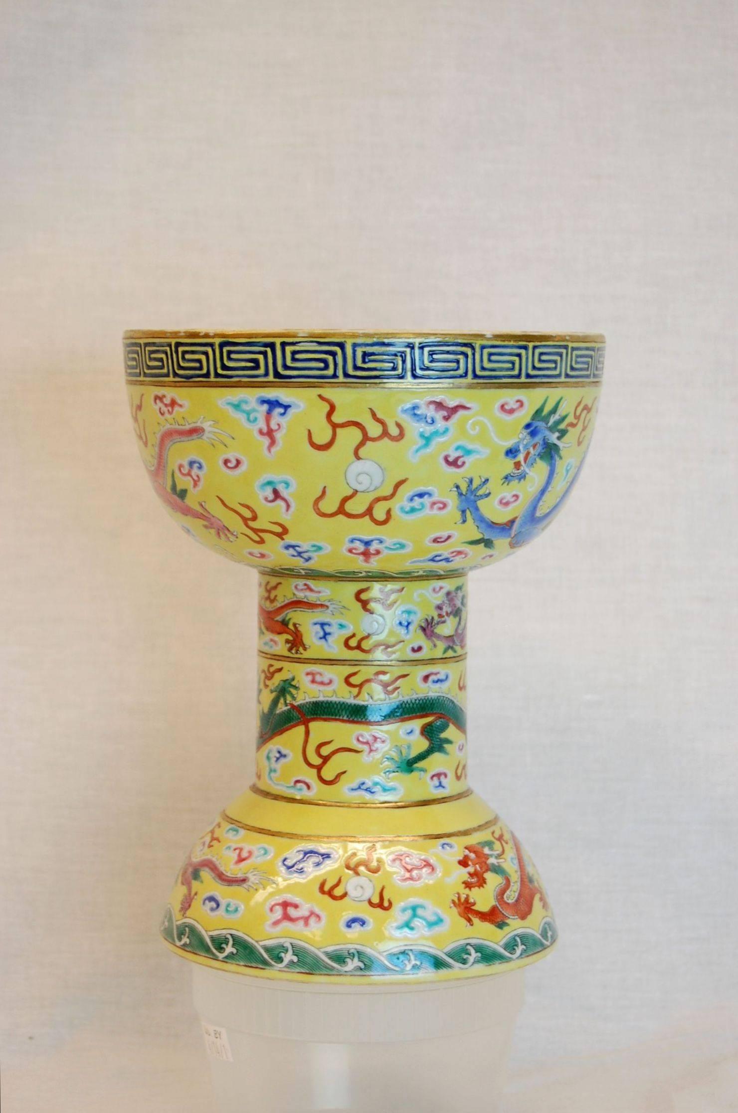 An early 20th century cup in a green/ yellow background decorated with dragons of various colors and shapes encircling the three areas of the cup.