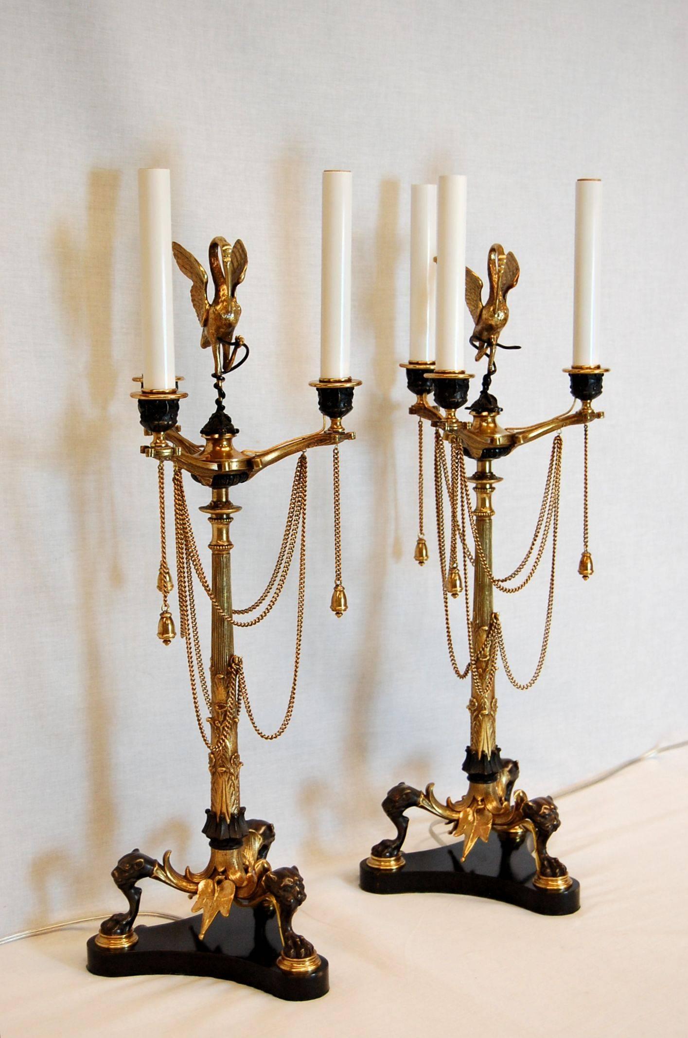 Pair of Renaissance Revival gilt bronze three-light candelabra with a beautiful bird sitting atop a thin bamboo-like leafy column stem with chains hung, in oil lamp form. Tripod legs with lion’s heads and paw feet on concave-sided metal base. Just