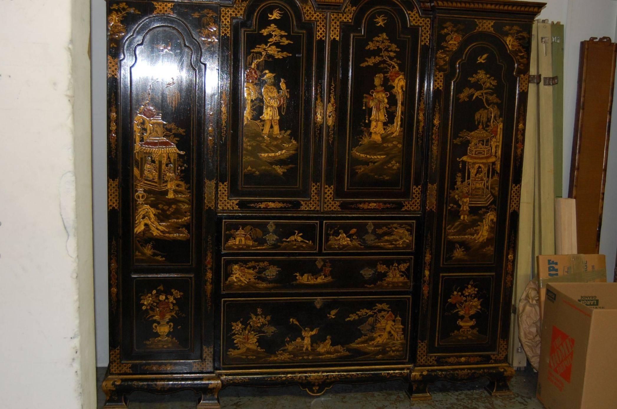 A Japanned wardrobe cabinet with original Chinoiserie decoration, two long cabinets, and a pair of center arched doors above a bank of four drawers. English, decorated in Chinoiserie landscape panels with raised gold lacquer detail. The end cabinets