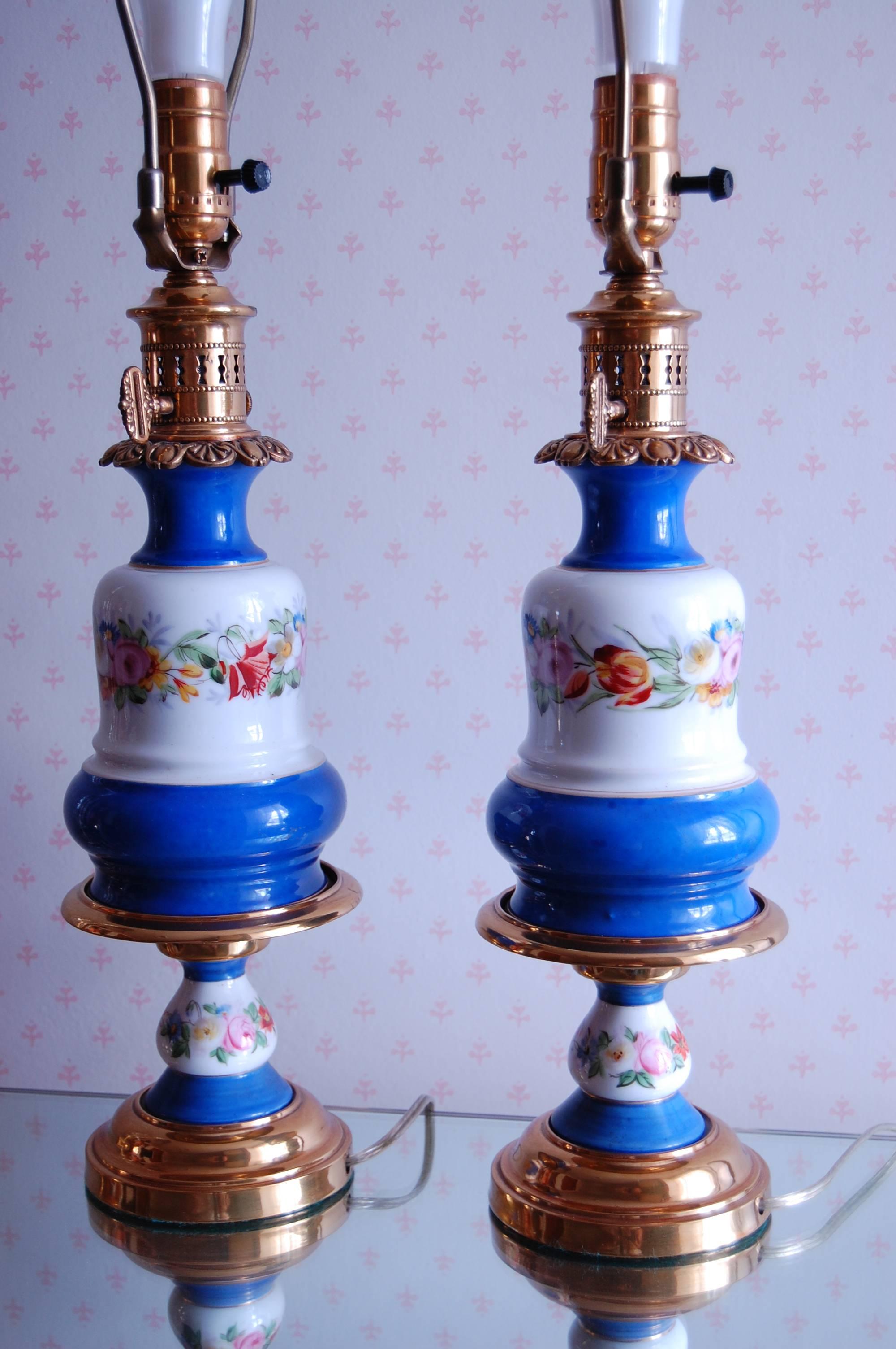 Pair of French oil lamps, circa 1850 with beautiful floral decorations on a white and blue background. It measures 14 inches to the top of the brass burner. Recently rewired with a three way socket, completely cleaned, polished and lacquered.