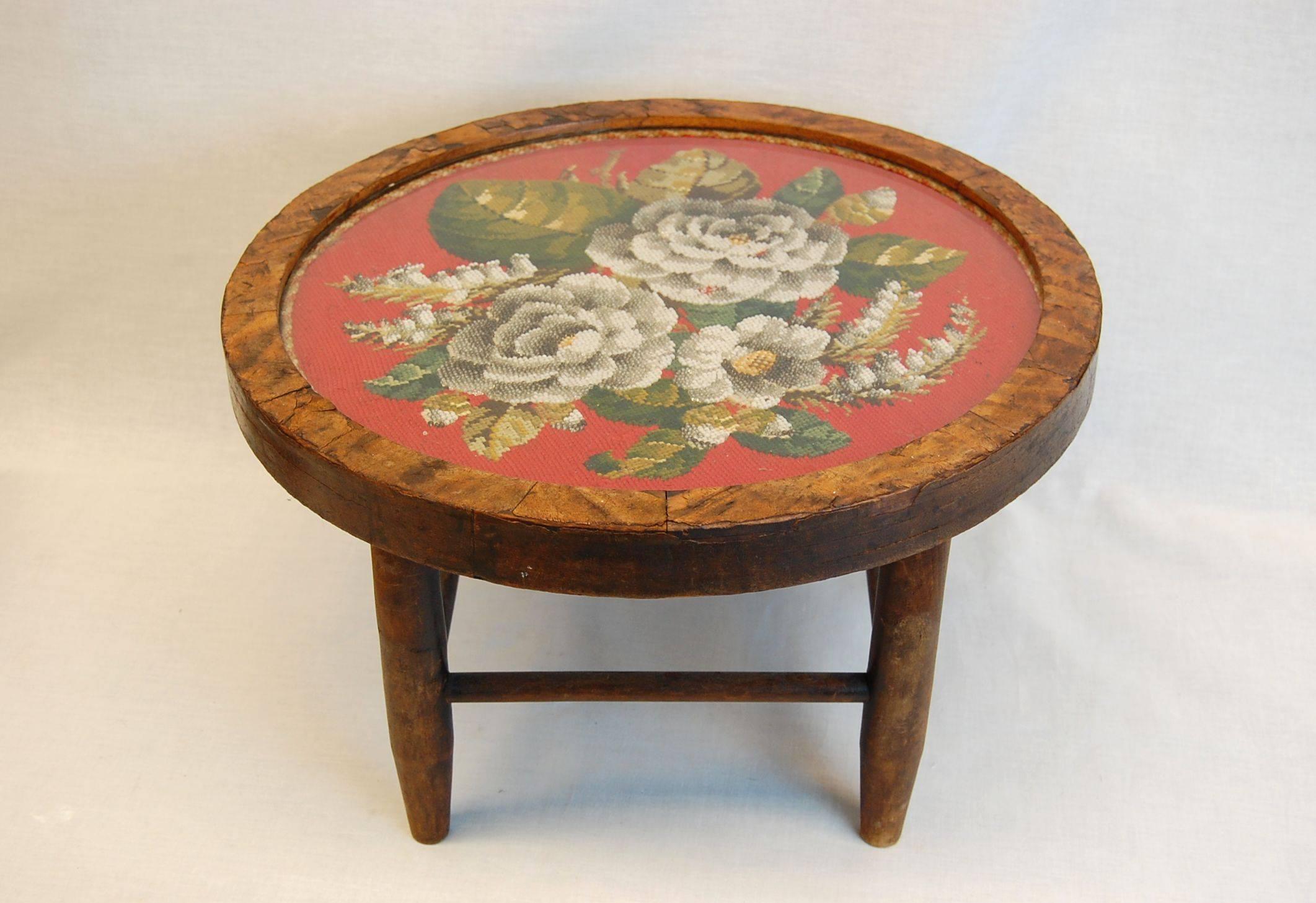 A circular floral needlepoint with clear and colored glass beads mounted in its original wooden frame under glass. It has been mounted onto a later made base, this could always be removed and used as a wall hung circular frame. Needlepoint is in