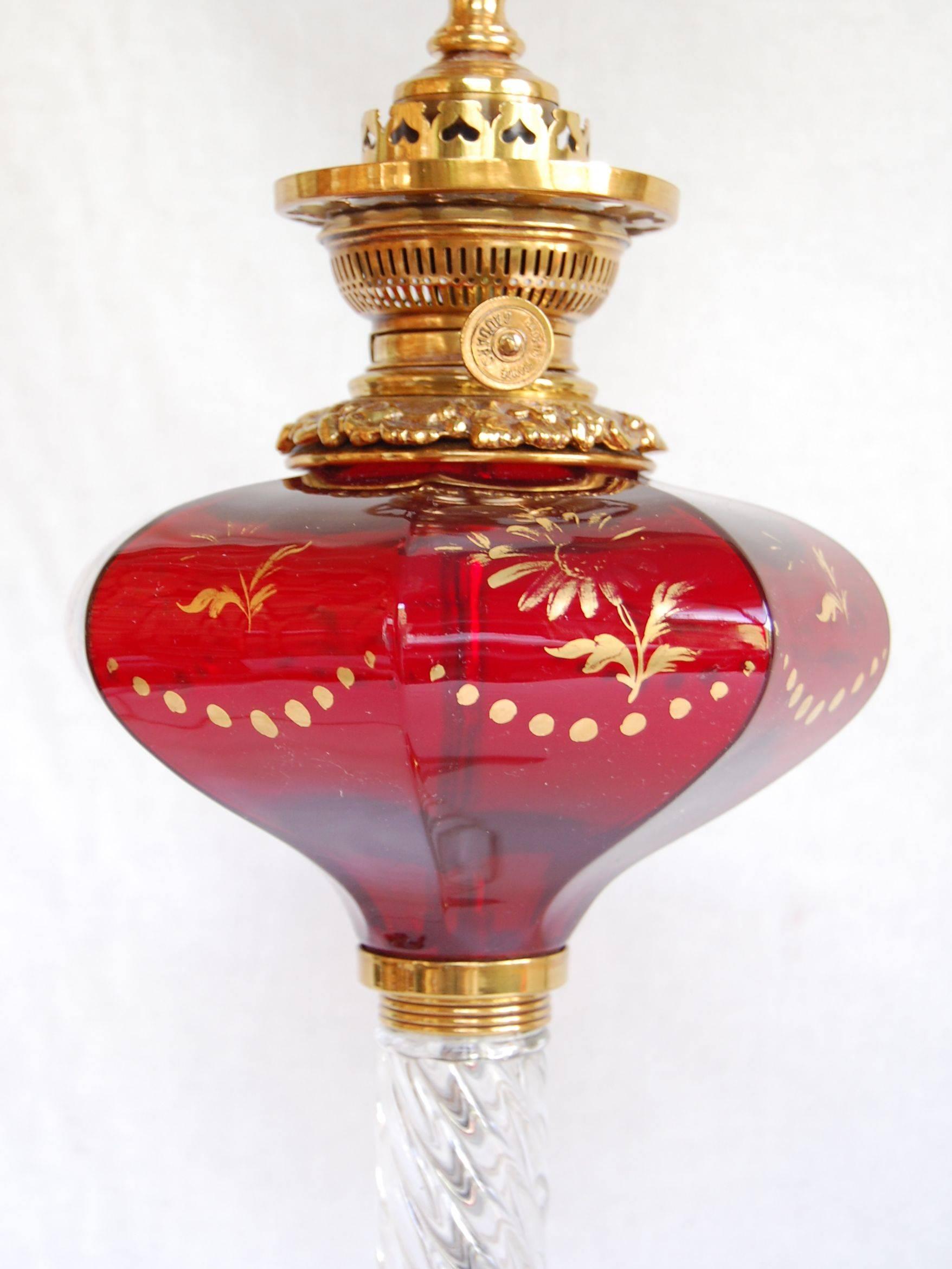 Mid-19th century ruby glass font oil lamp with gold floral decorations and a clear, twisted glass column and base. Cleaned and rewired with a three-way socket. 20 inches to the top of lamp, 30 inches to the shade rest. American or English, possibly
