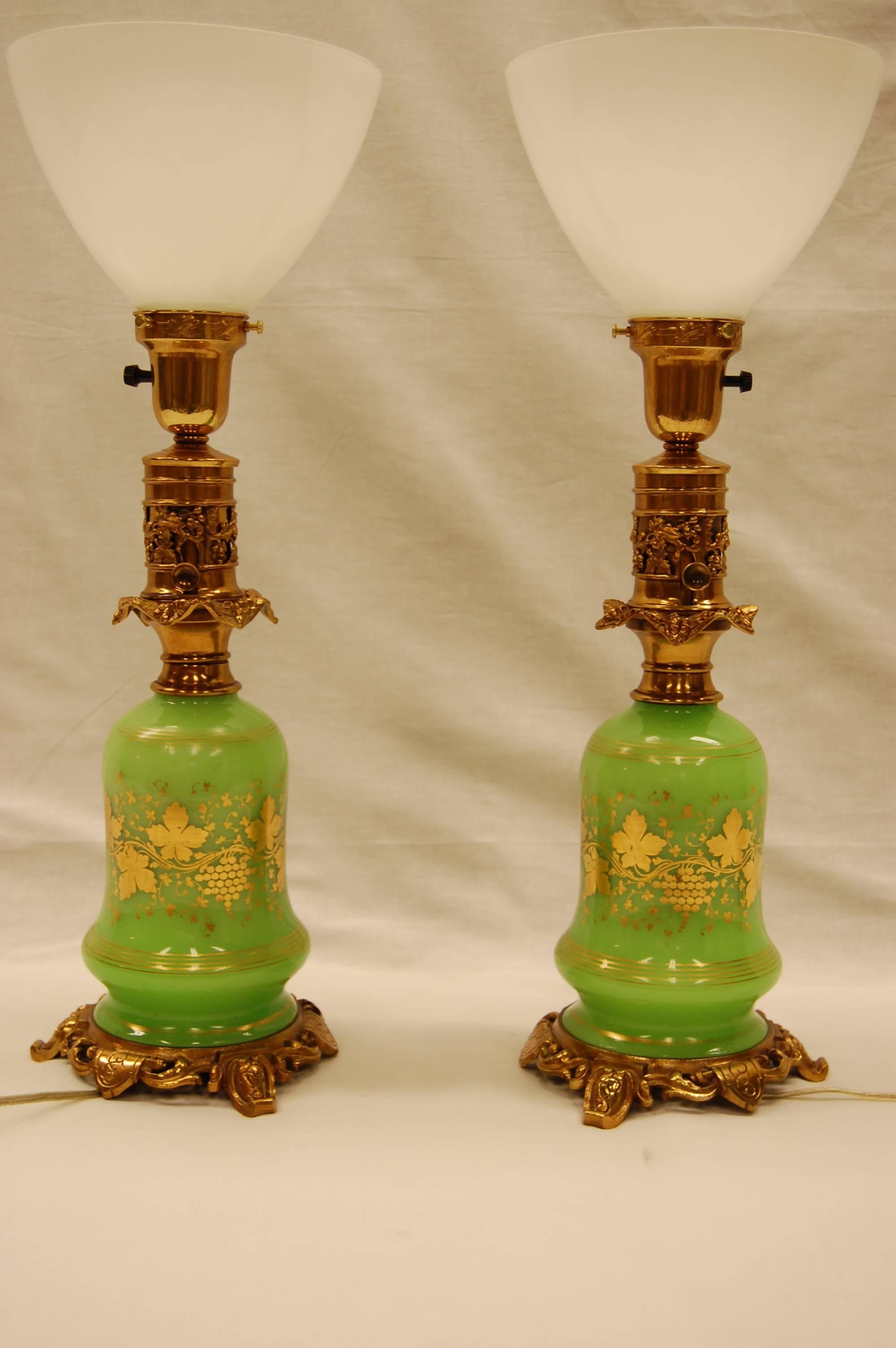 Pair of opaline oil lamps with gold leaf grape leaf decorations, recently rewired with three-way sockets. Completely cleaned and lacquered brasses. Measure: 14 inches to the top of the oil font. With original brass fittings.