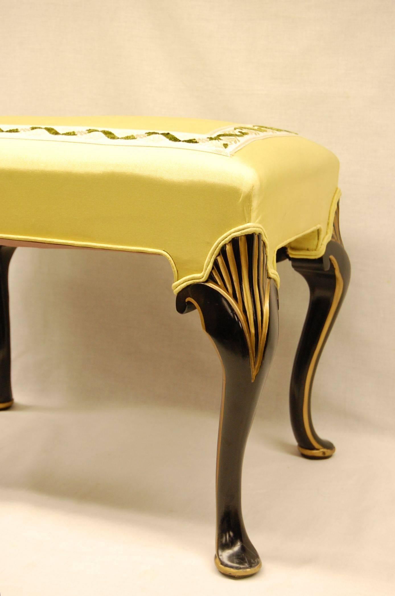 Bench in excellent condition covered in yellow moire fabric with a braid on the top surface. Black painted legs with gold accents.