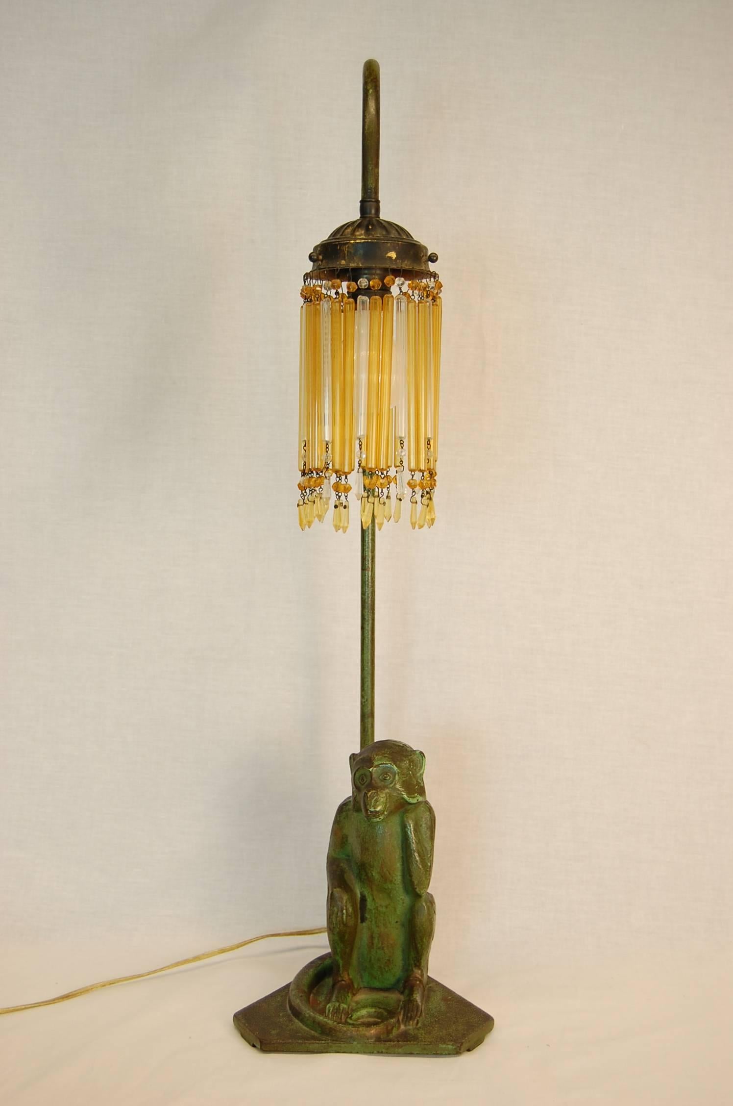 Wonderful cast metal figure of a monkey on a base wired as a lamp with amber glass prisms in a modeled green painted finish. Recently wired.