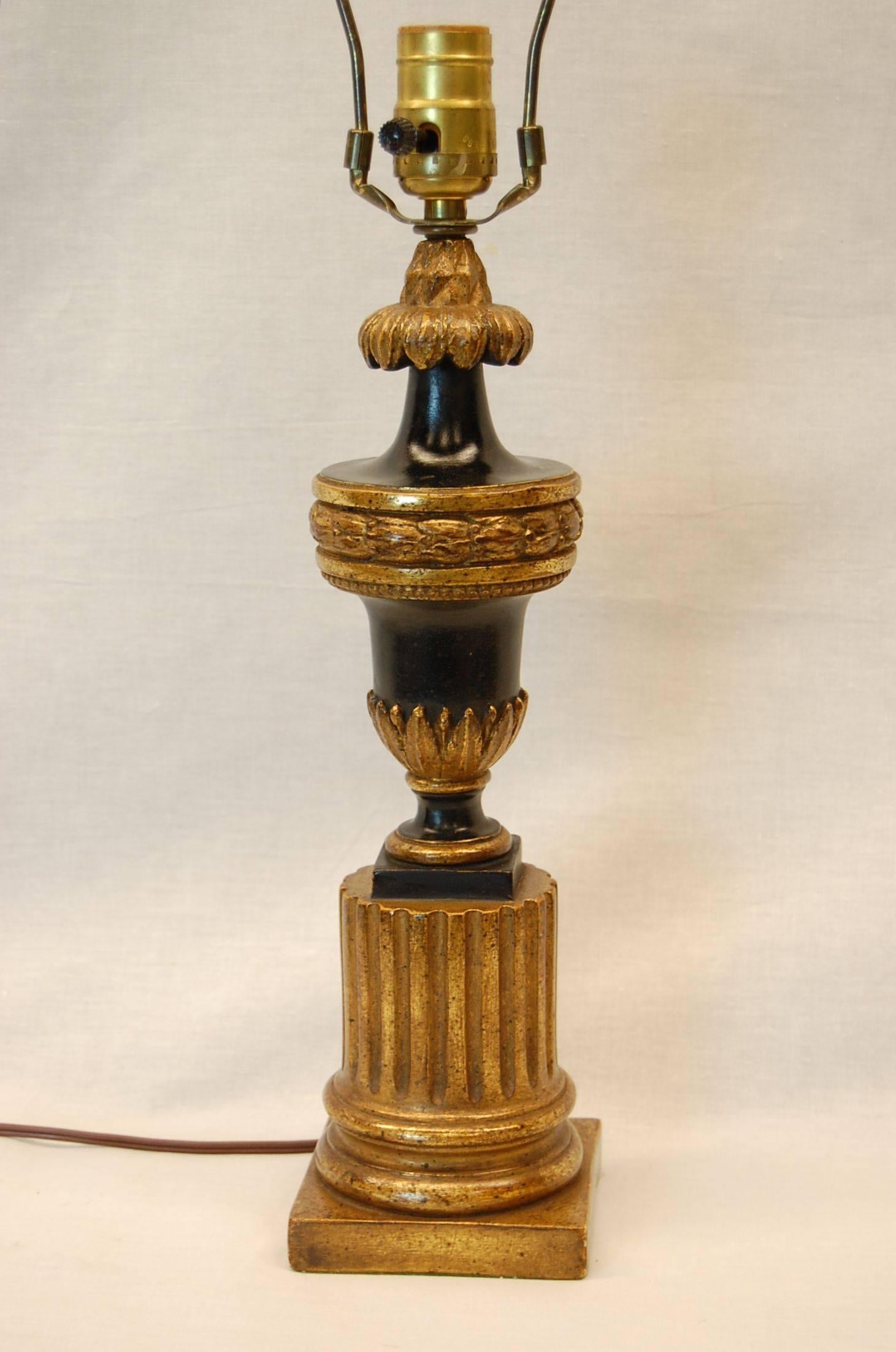 Mid-Century nicely carved wooden urn lamp is in black paint and gold leaf, wired with a three way socket. 22 inches to the shade rest, the urn stands 14 inches tall.