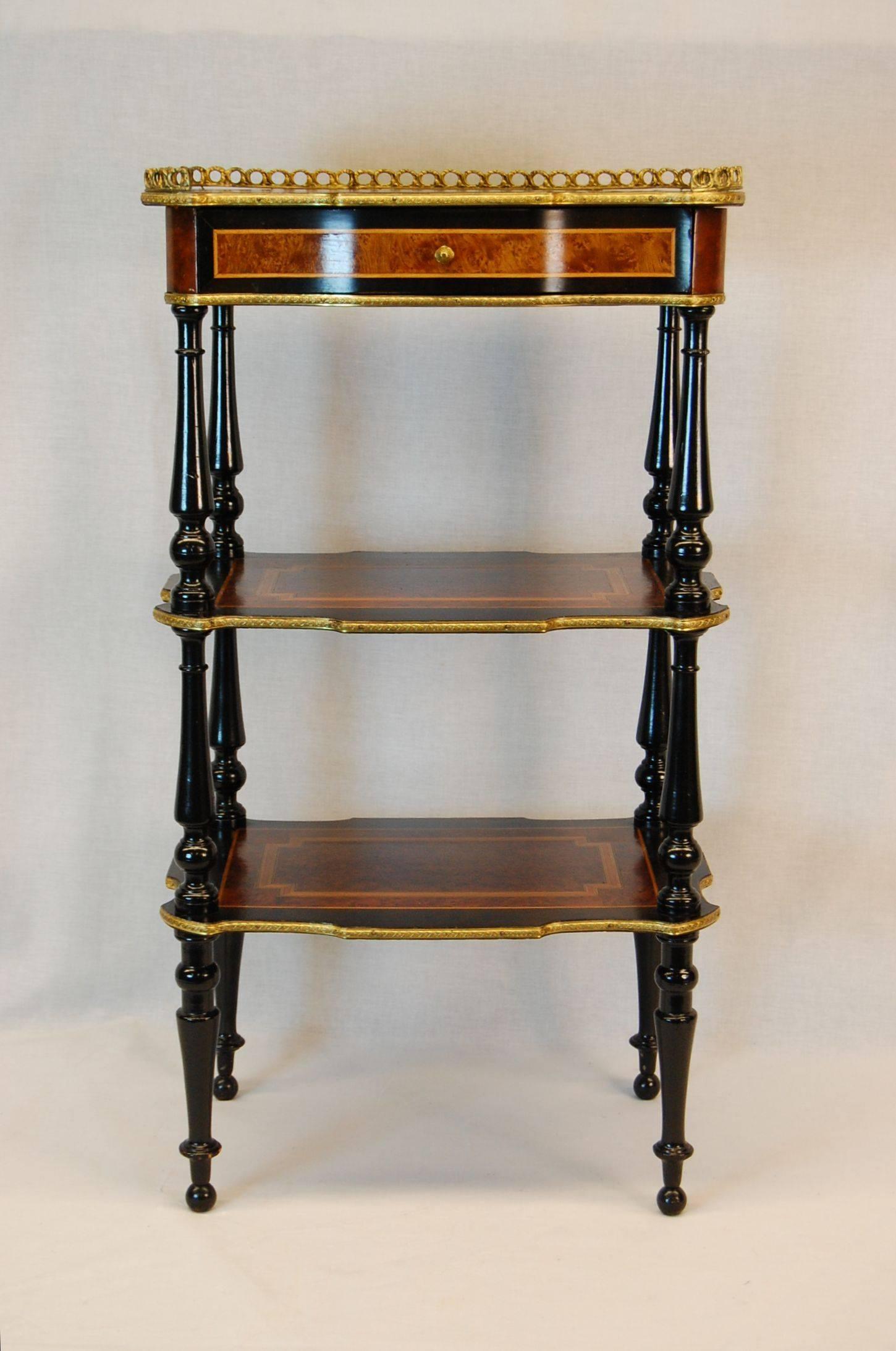 Ormolu galleried and trimmed triple-tiered table with turned ebonized legs. Complex veneers, bandings and inlays of burl, rosewood and satinwood. 
