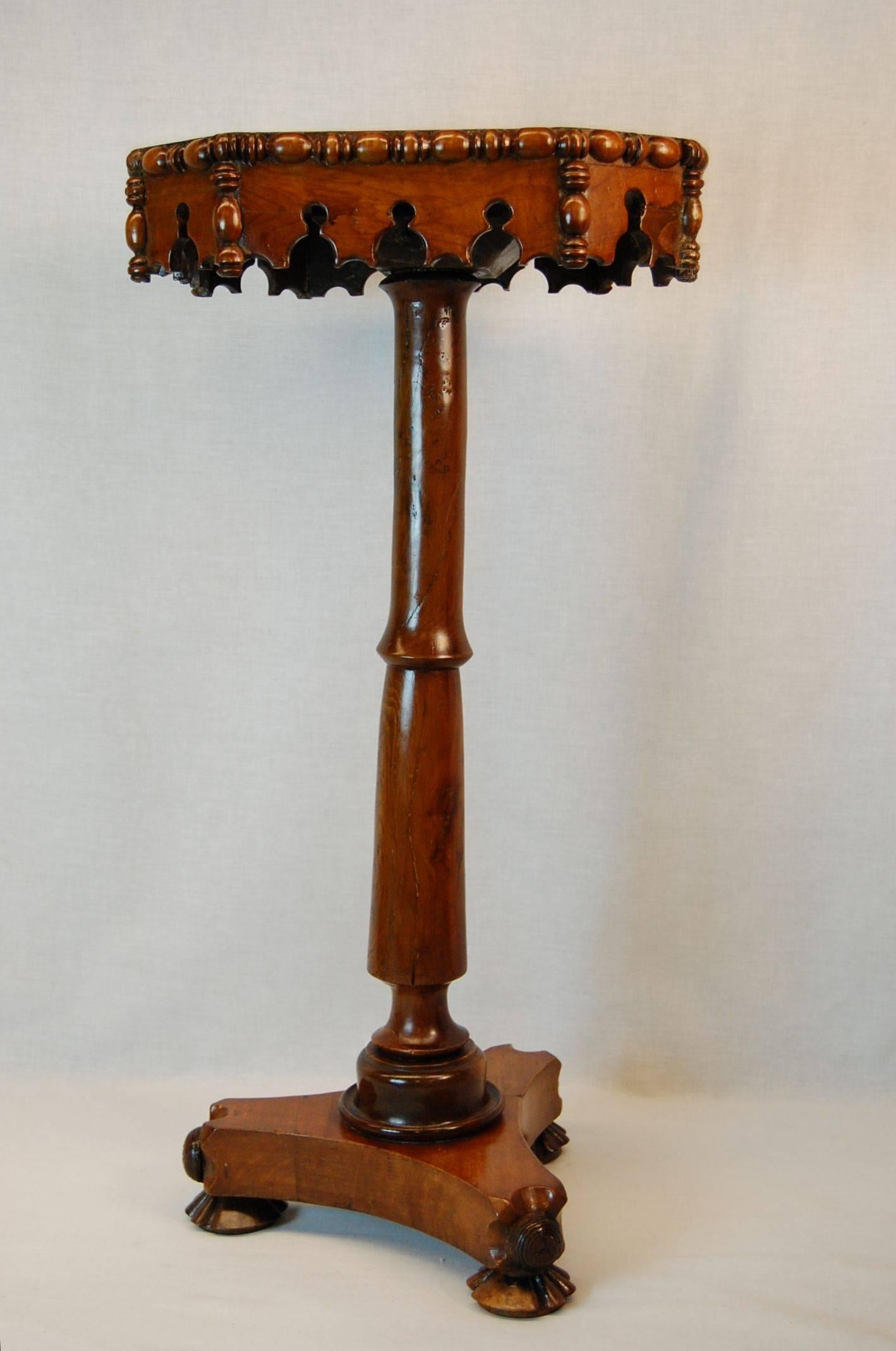 A William IV candle stand with octagonal top above a turned column, a Gothic themed apron with Egg and Turned wood designed molding surrounds the top and apron edges. The tripod base terminates in three circular carvings and rests upon circular