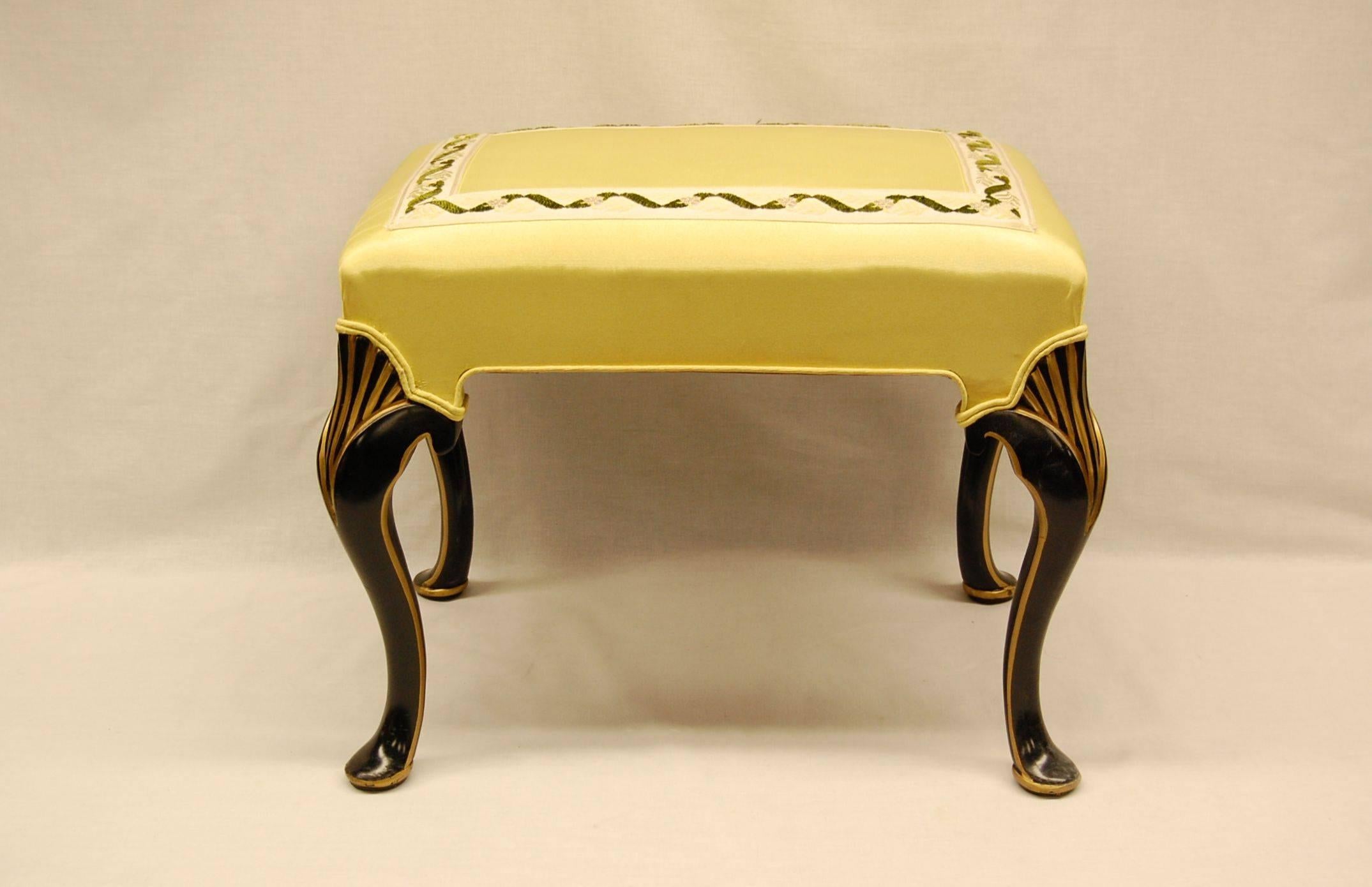 Bench in excellent condition covered in yellow moire fabric with braid on the top surface. Black painted legs with gold accents.