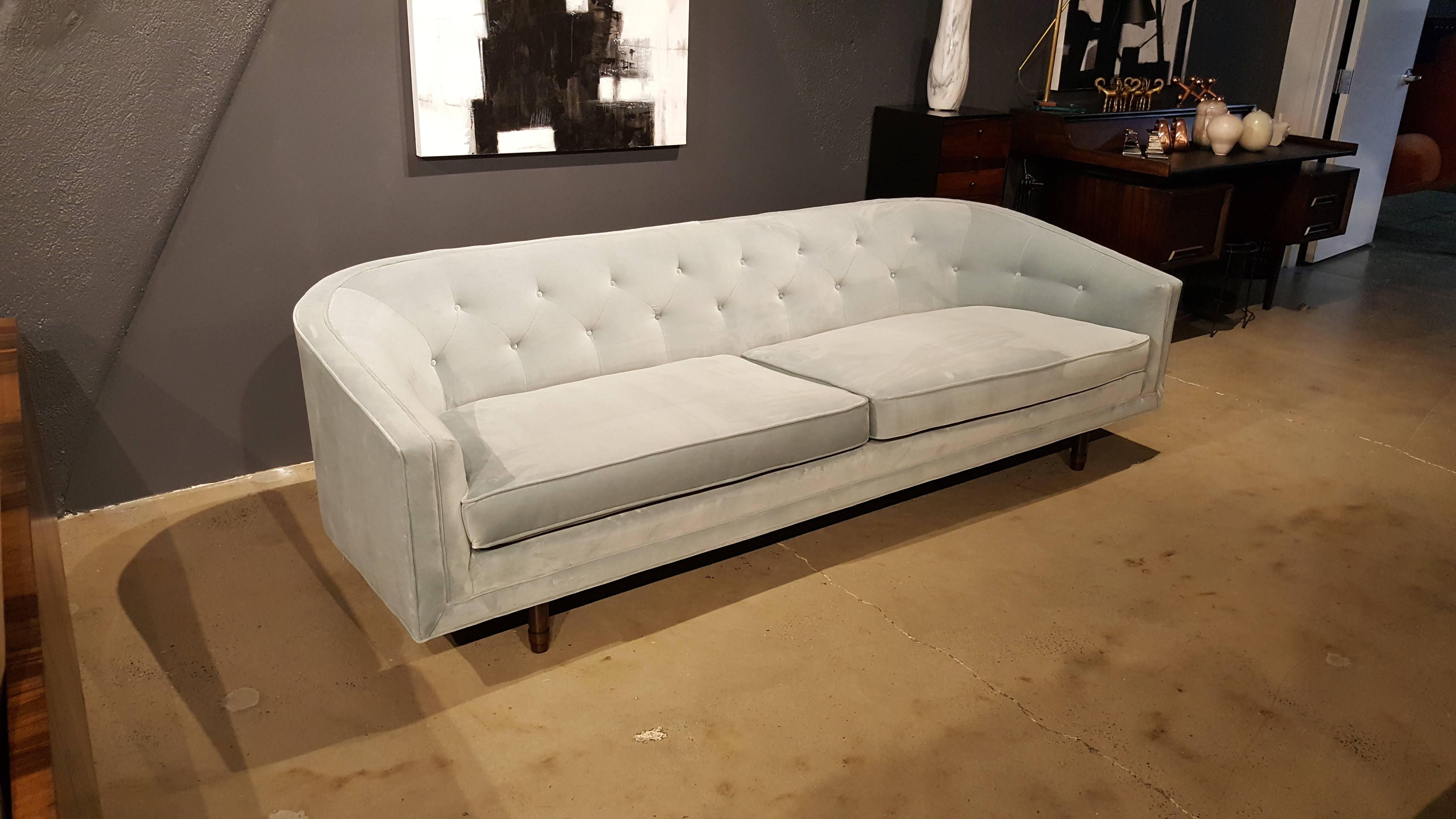 Elegant, sleek sofa by Selig in pale dove blue grey cotton velvet with exposed walnut legs. Beautiful button tufting detail gives this piece the feeling of a Danish Modern Chesterfield quite lovely. Clean lines and gorgeous curve from back to arm.