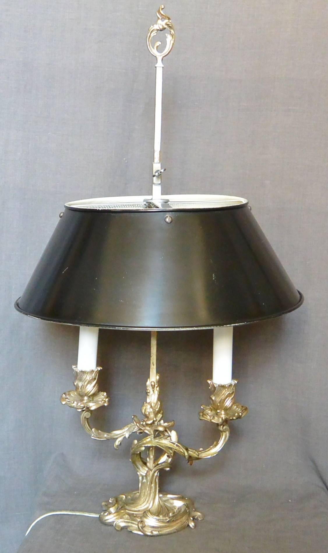 Lampe bouillotte à deux bras de style Louis XV en métal argenté avec abat-jour en tole noire postérieur. Nouvellement électrifié, France, vers les années 1930. 
Dimension : 23.5