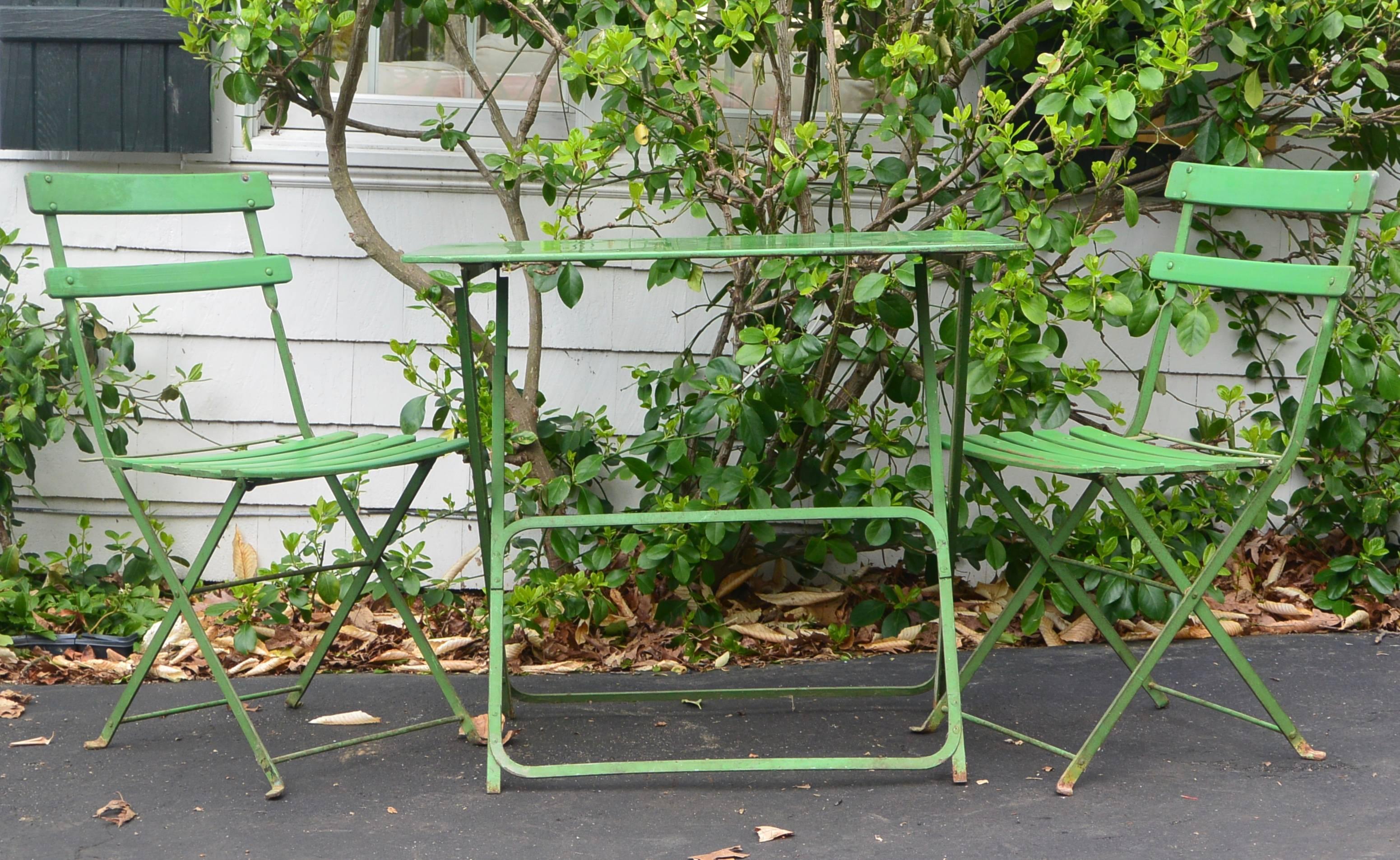 Vintage French metal bistro table and chairs in green folding metal with wood slatted seats, France, circa 1940s. 
Dimension estimates: table 30' H x 36' x 24'; chairs 32' H back x 18' W seat.