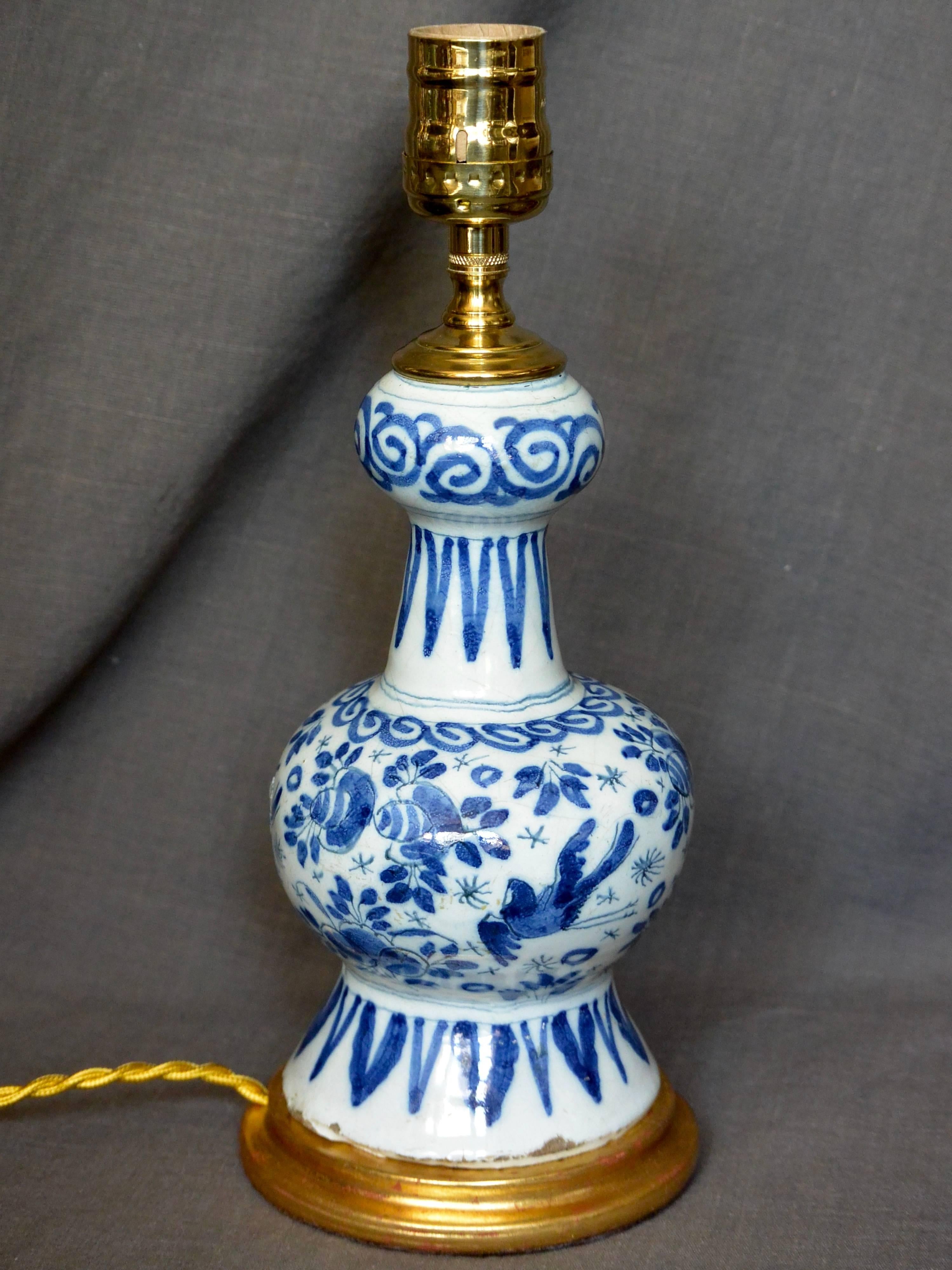 Lampe vase Delft hollandaise bleue et blanche sur base dorée à l'eau. Petit vase en faïence de Delft de forme balustre à décor floral délicat, oiseaux et bordures, monté en lampe sur base dorée à l'eau avec cordon et interrupteur en soie dorée.
