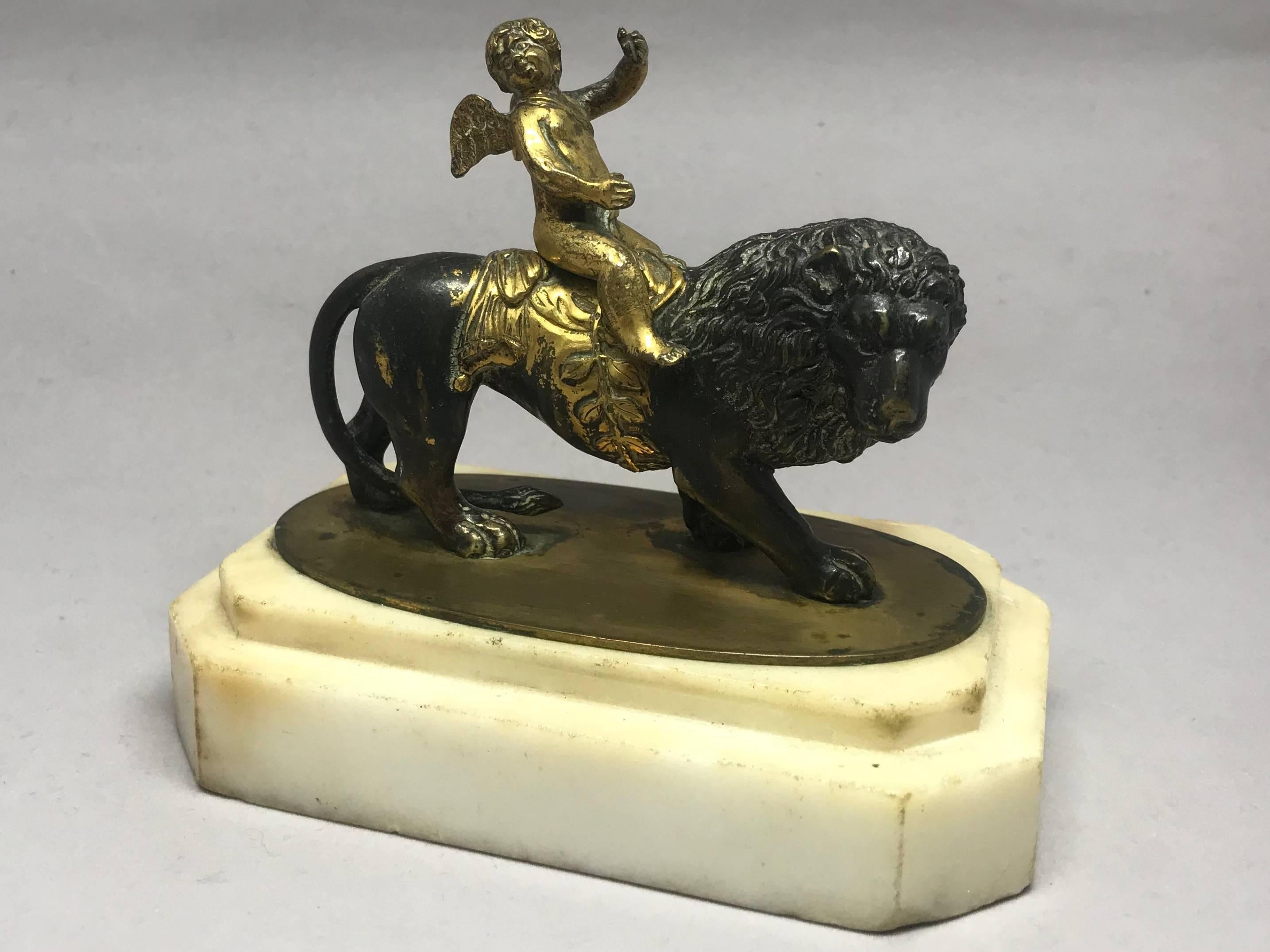 English Regency gilt bronze cupid and lion paper weight sculpture.  Patinated bronze and ormolu cast and chased cupid and lion with gilt saddle and laurel girth on a rectangular Carrara white marble base. Attributed to Thomas Weeks, London.