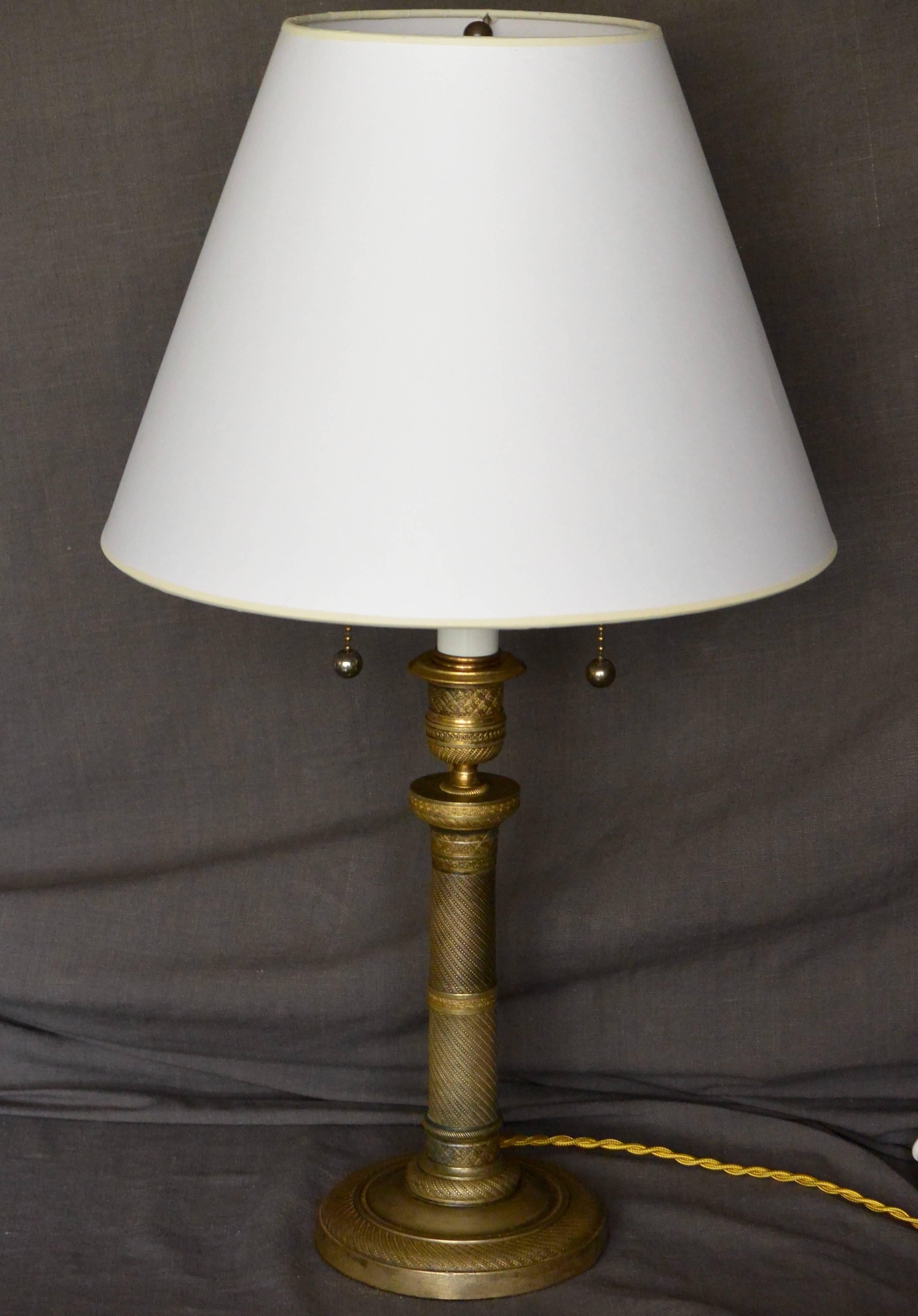 Charles X gilt metal candlestick lamp. Charles X gilt metal candlestick mounted as a lamp, newly re-electrified with two lights in gold silk cord and switch.  France, circa 1830. 
Lampshade is optional and not included.  
Dimensions: 5