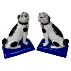 Pareja de figuritas de porcelana de un carlino sobre peanas azul cobalto, finales del siglo XIX