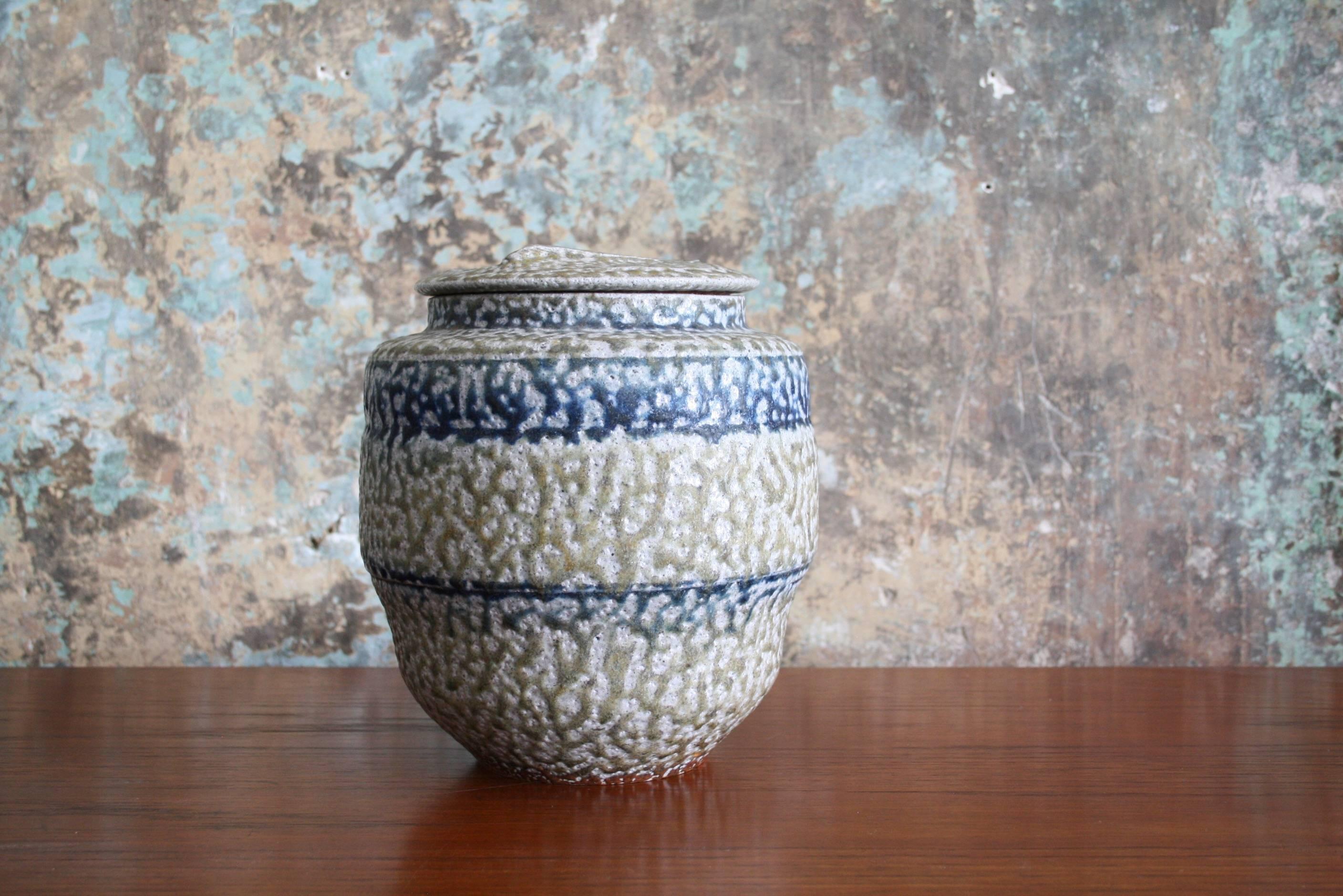 A salt-glazed, functional lidded stoneware vessel by highly regarded ceramic artist Karen Karnes (American, 1925-2016). This fluted round vessel includes a removable domed lid and features a beige body with cobalt blue stripes and an overall white