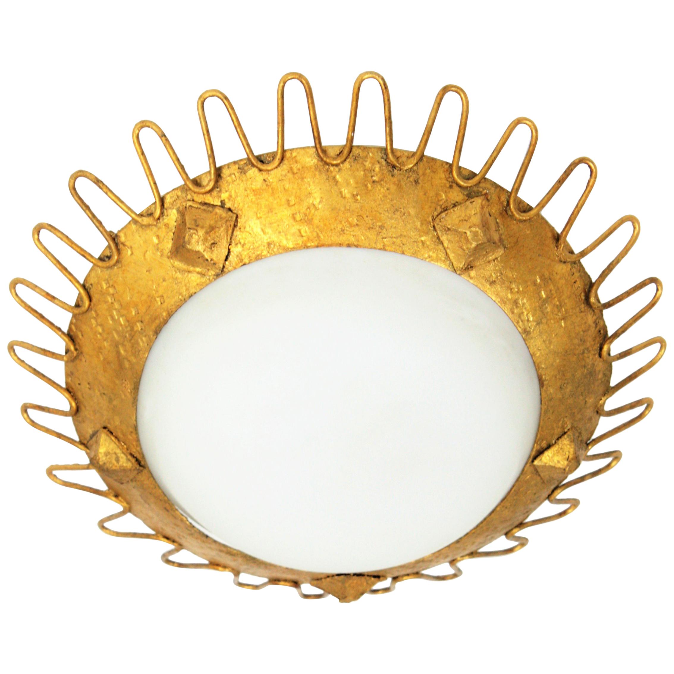 A Brutalist style hand-hammered iron and opaline glass sunburst flush mount manufactured at the Mid-century Modern period. This light fixture has a  looped edge, rhombus decoration on the frame and gold leaf finish. In the manner of Jean Royère.