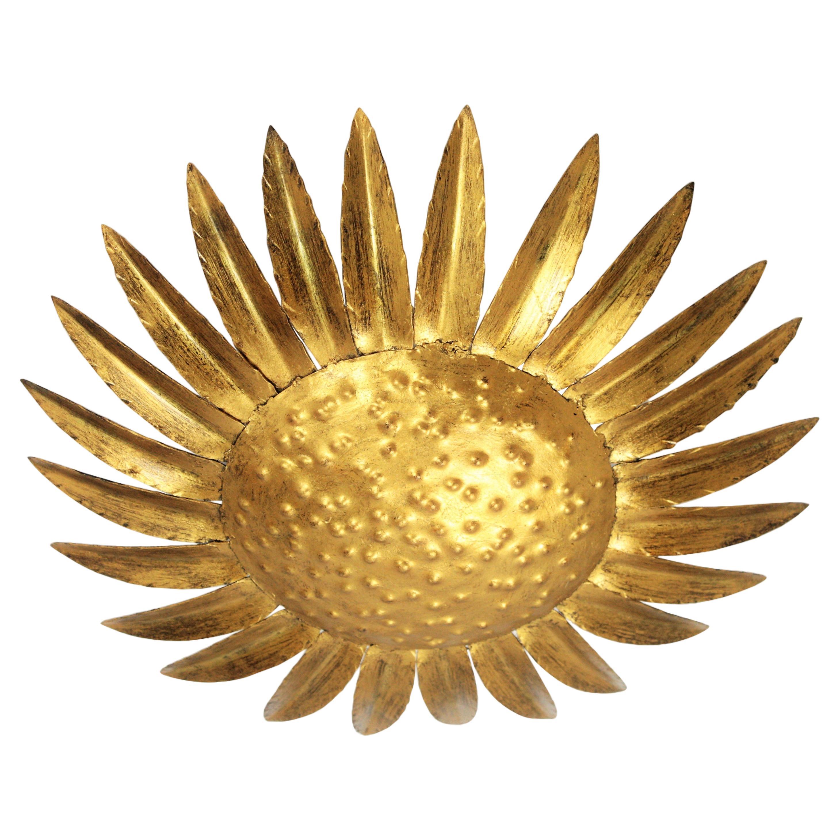 Mid-Century Modern hand-hammered iron sunburst / sunflower shaped light fixture, Spain, 1950s.
Manufactured by Ferro Art.
It has a textured hand-hammered decoration in the central part and gilded finishing.
It can work as a ceiling light fixture or