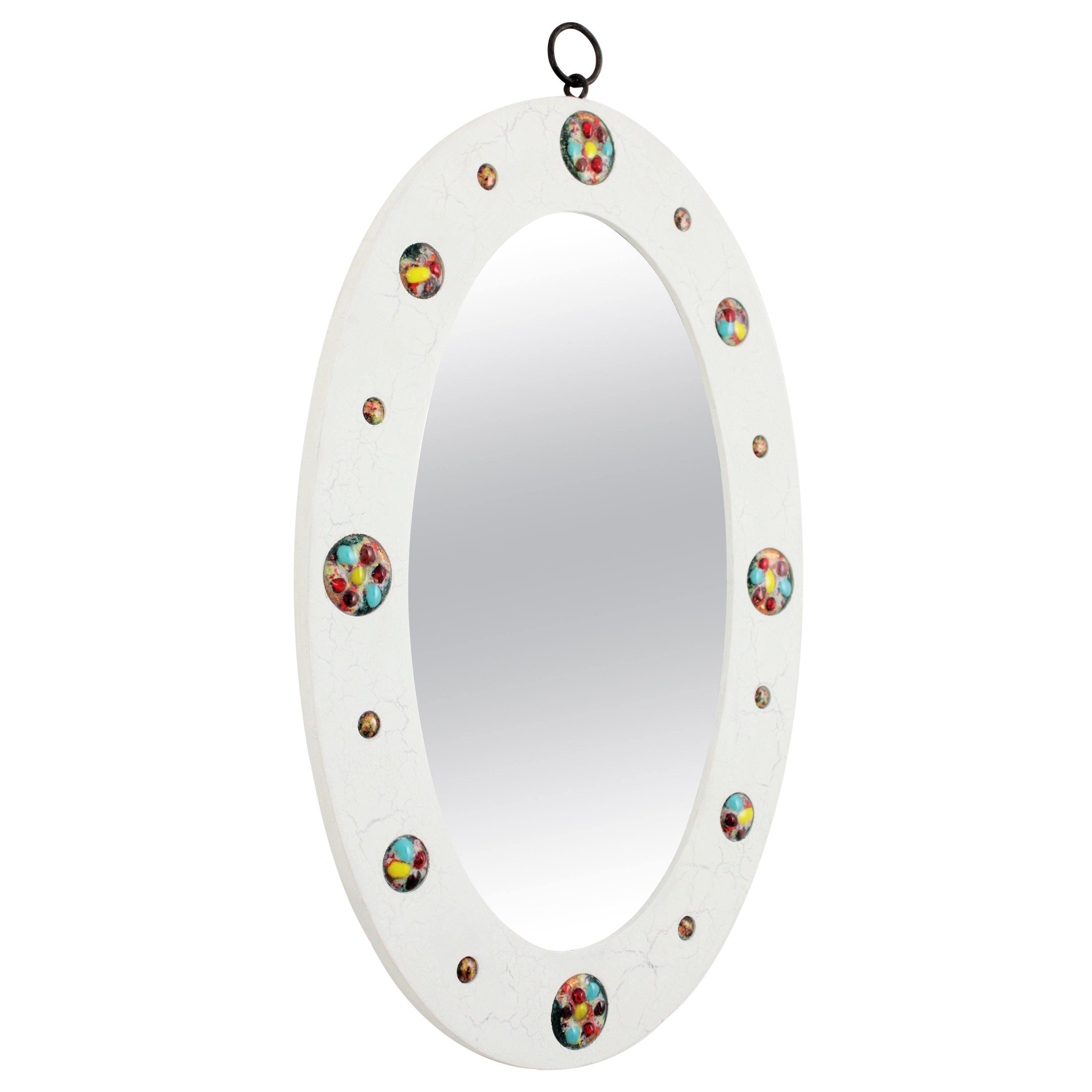 Mid-Century Modern wood and enamel oval mirror with white cracked patina. Spain, 1960s.
A beautiful oval shaped white patinated mirror with cracked effect and colorful enamel-on-copper circular pieces decorating the frame and an iron ring to hang