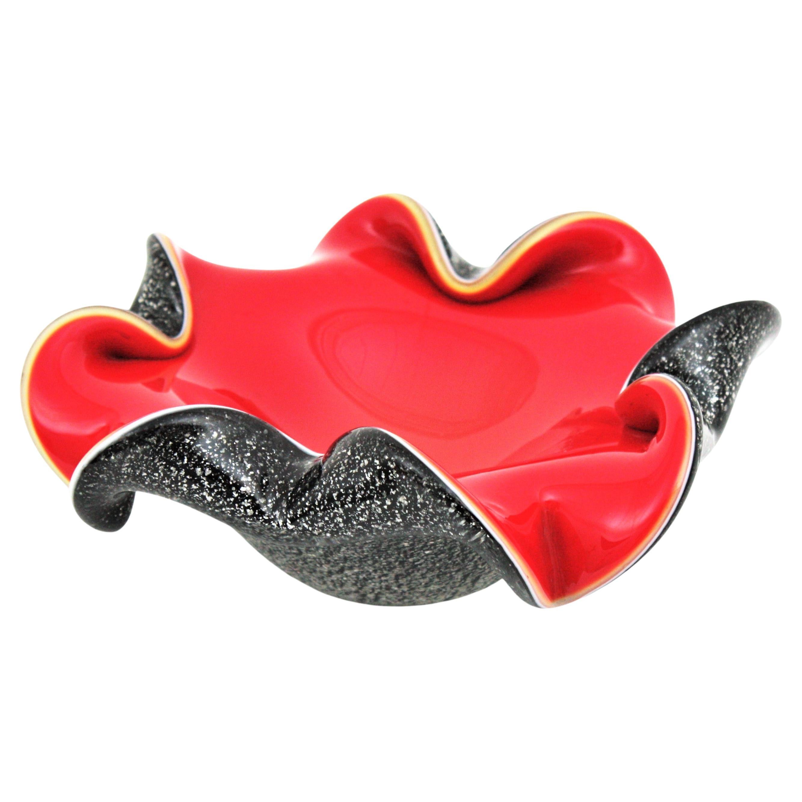 Colorful flower shaped Murano art glass bowl with silver flecks in red and black glass cased into clear glass. Attributed to Seguso Factory, Italy, 1950s.
This heavy hand blown glass bowl has a design in flower shape with folded rims full of